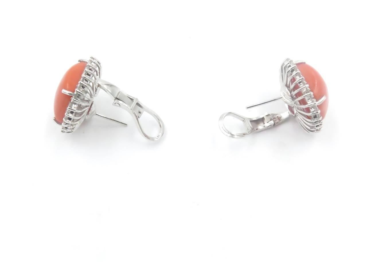 An 18 karat white gold, coral and diamond earrings. Circa 1990. Each set with a square cabochon coral, measuring approximately 14.00 x 14.00mm, within a circular-cut diamond surround. Fifty six(56) diamond weigh approximately 1.00 carat. Length is
