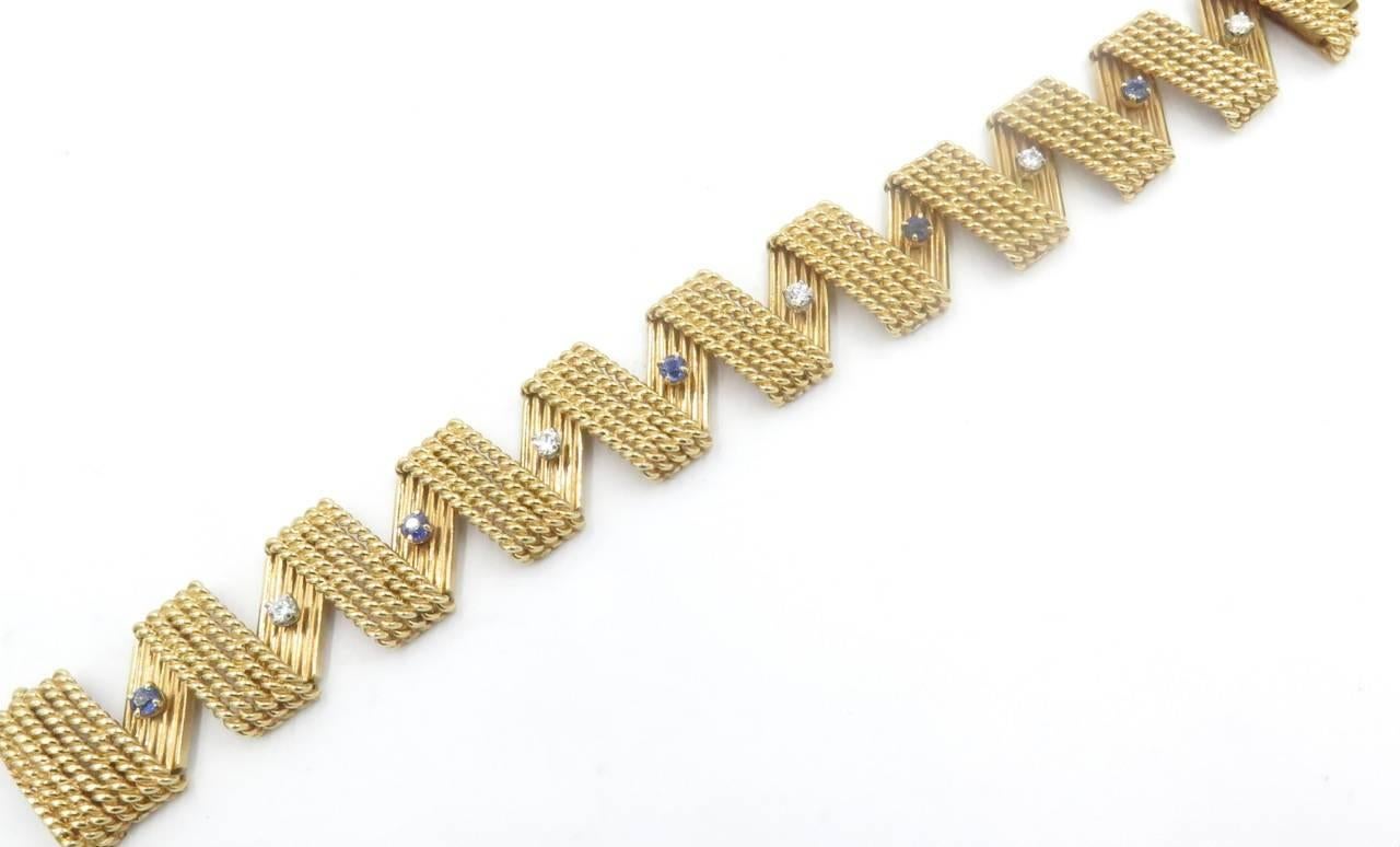 A 14 karat yellow gold, diamond and sapphire bracelet. Circa 1960. The flexible bracelet of zig zag design, the links designed as rope work and fluted panels, set with circular cut diamonds and sapphires. Five (5) diamonds, weigh approximately 0.60