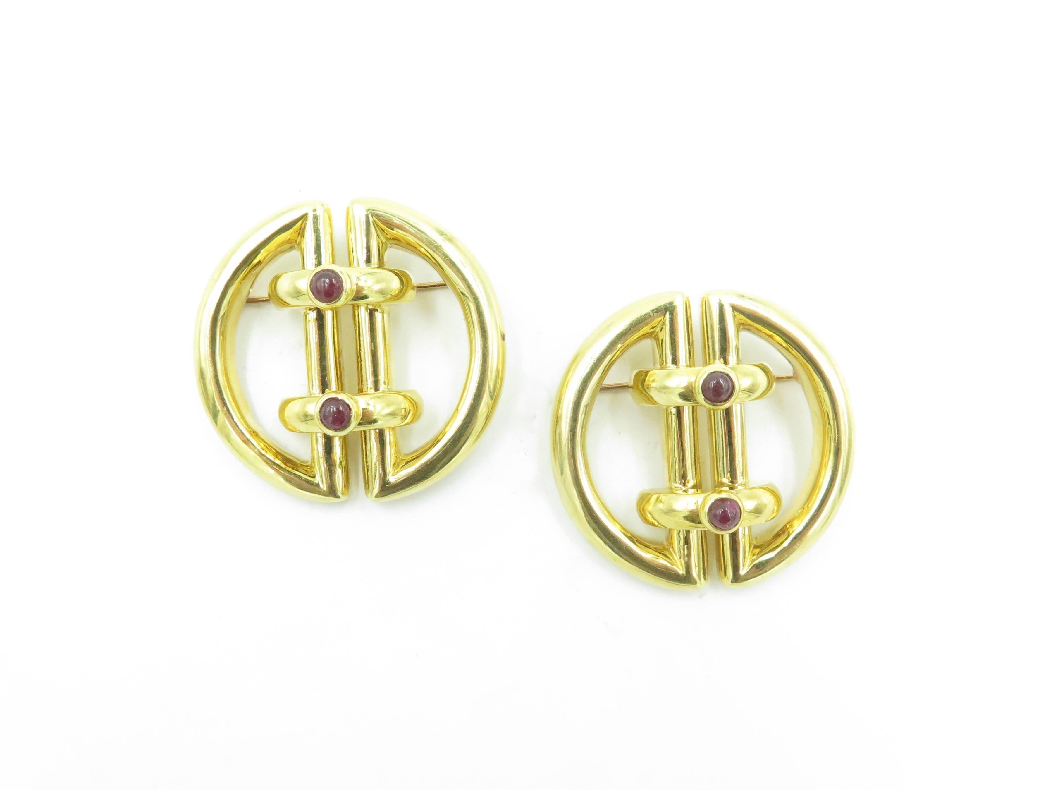 A pair of 18 karat yellow gold and ruby clip brooches. Tiffany & Co. Circa 1970. Each of polished gold buckle design, enhanced by cabochon rubes. Diameter is approximately 1 1/2 inches. Gross weight is approximately 54.2 grams. Stamped Tiffany &