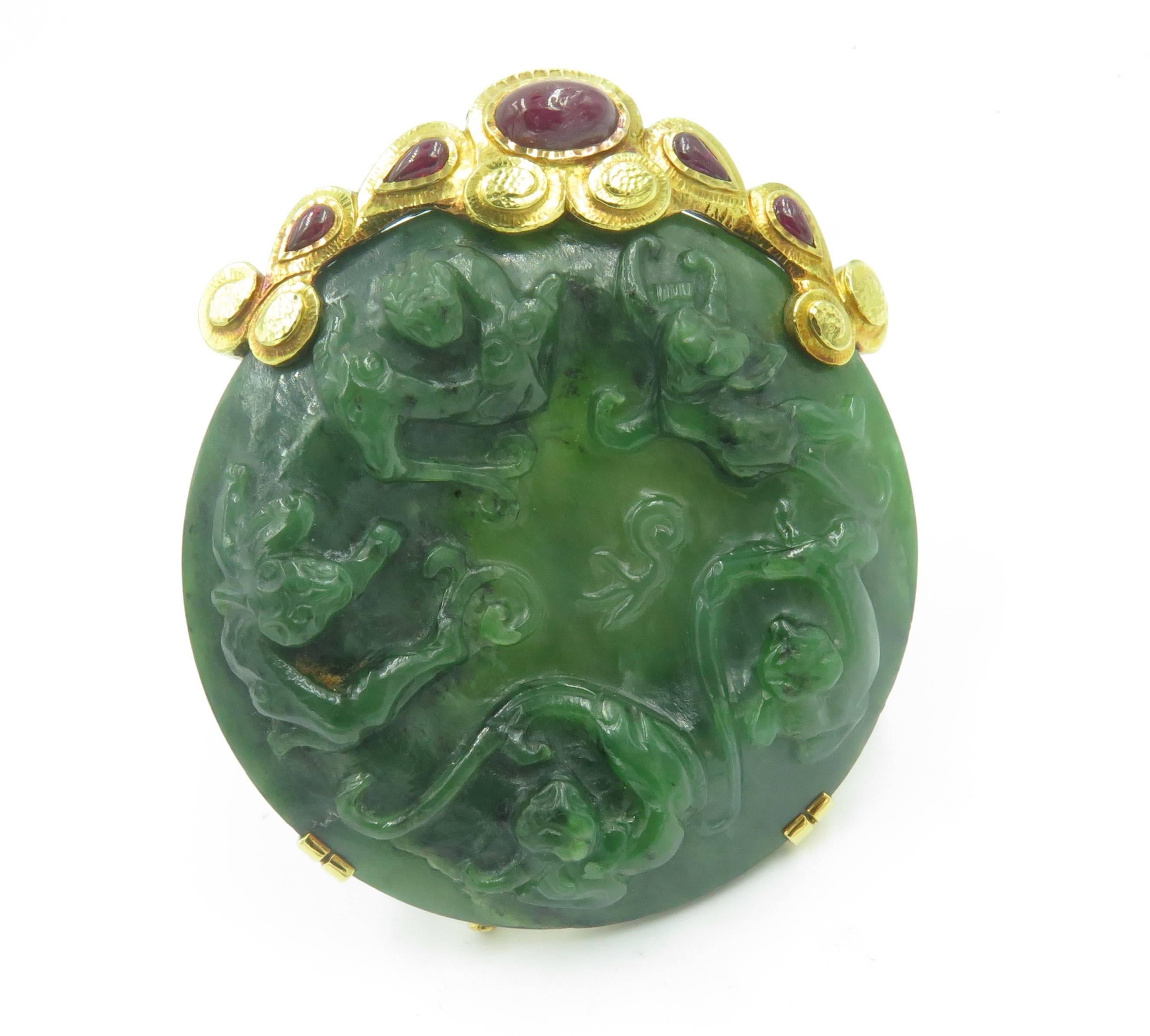 An 18 karat yellow gold, jade and ruby brooch. David Webb. 1971. Designed as a carved jade disc, enhanced at the top with a scrolling hammered gold frame, set with oval and pear shaped ruby cabochons. Brooch measures approximately  3 1/2 inches.