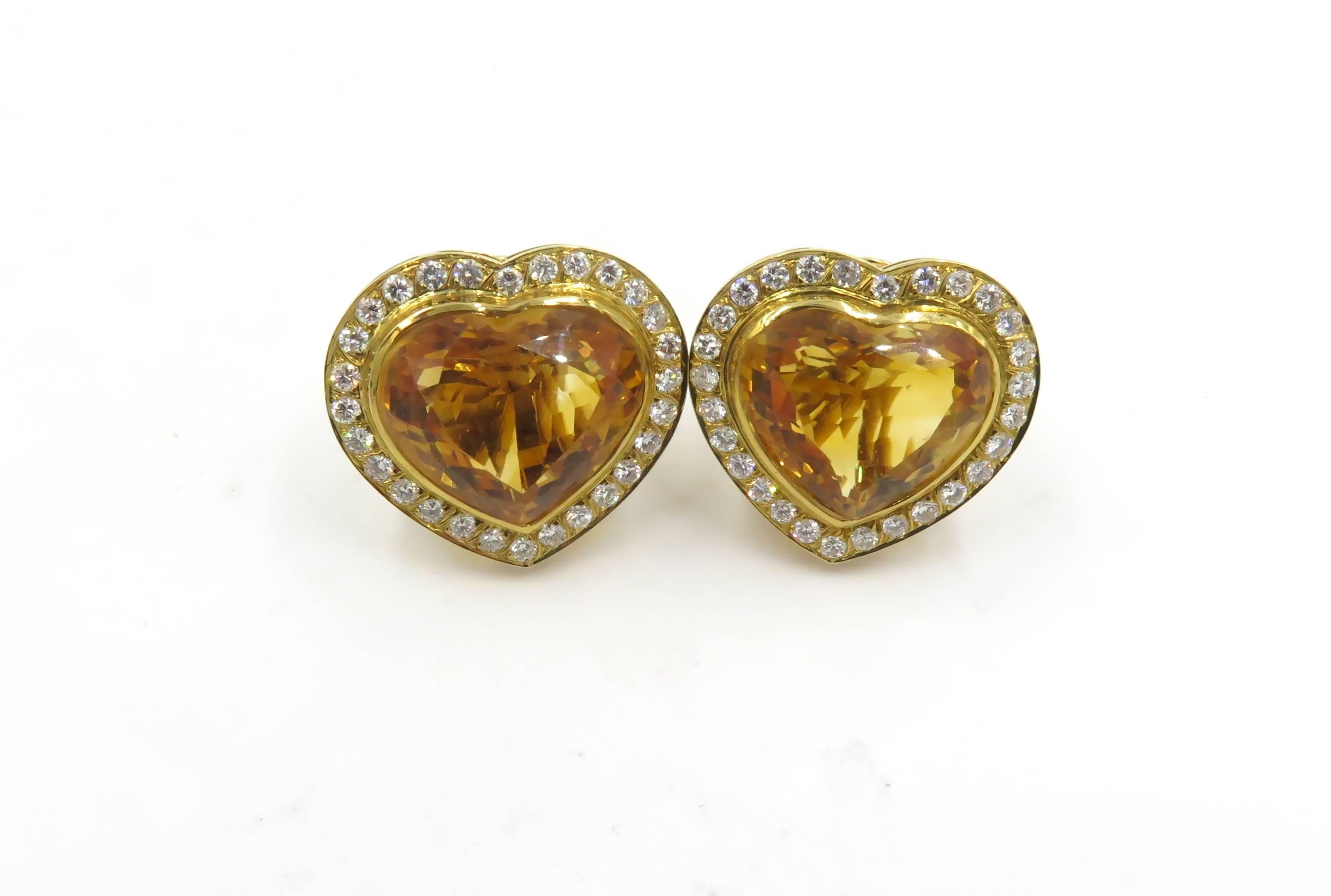 A pair of 18 karat yellow gold, citrine and diamond earrings. Circa 1980. Each set with a heart shaped citrine, each measuring approximately 17.50 x 20.10 x 10.15mm, and weighing approximately 18.45 carats, within a circular cut diamond surround.