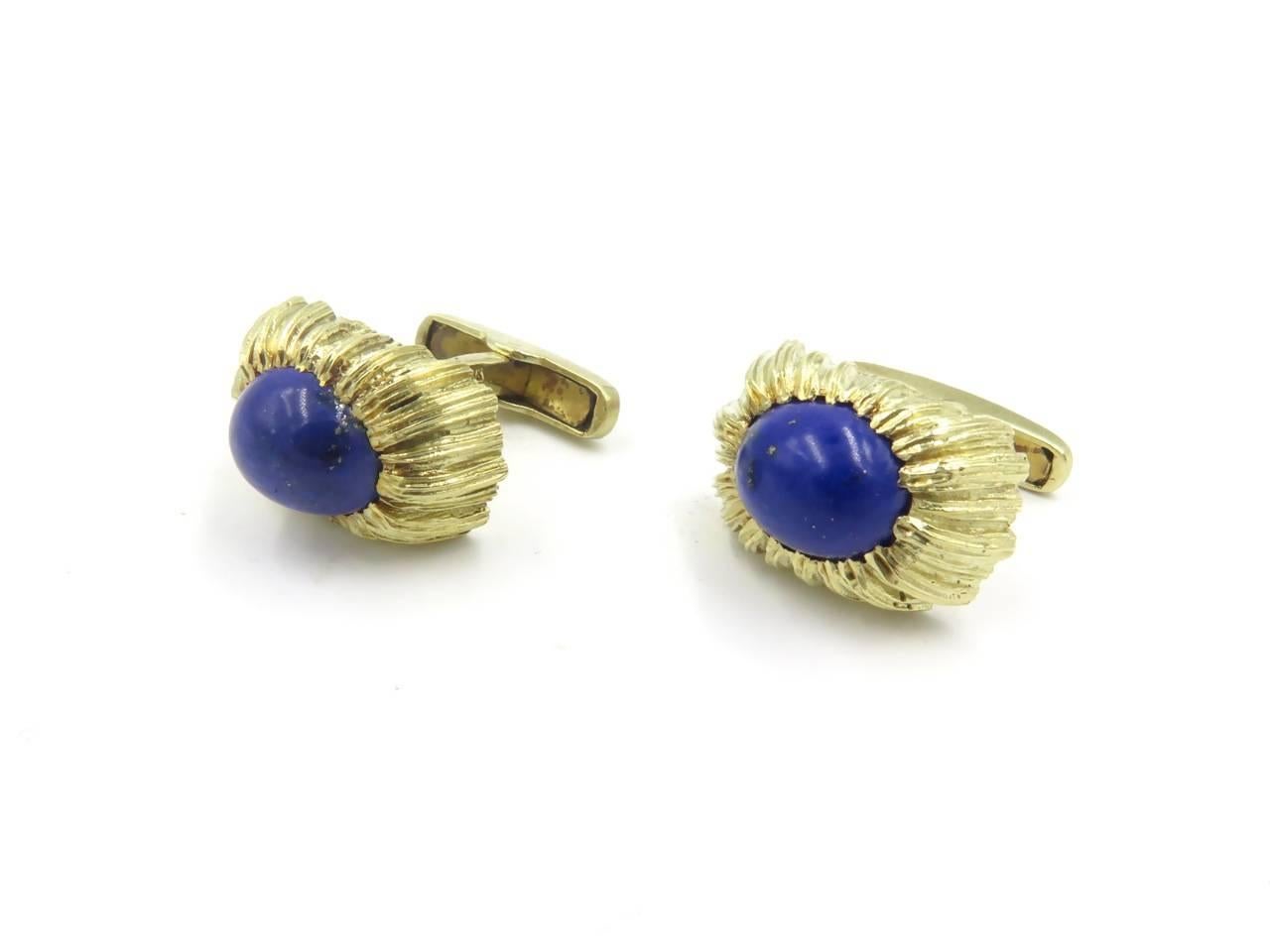 A pair of 14 karat yellow gold and lapis lazuli cufflinks. Each single link centering an oval cabochon lapis lazuli, measuring approximately 12.00 x 10.00mm, within a regular fluted and textured surround, joined by a bar to a swivel link. Length is