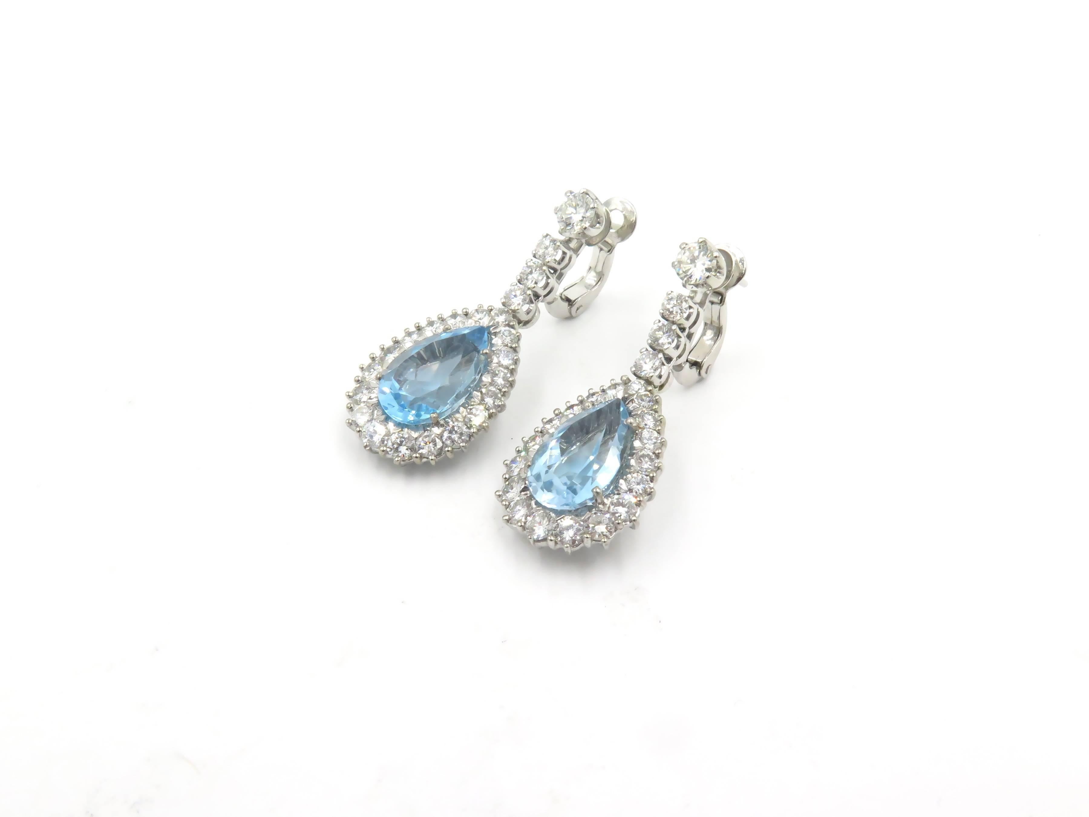 A pair of diamond 18 karat white gold and blue topaz earrings. Each suspending a pear shaped blue topaz, weighing approximately 5.00 carats. within a circular cut diamond surround, suspended from a circular-cut diamond line surmount. Forty six (46)
