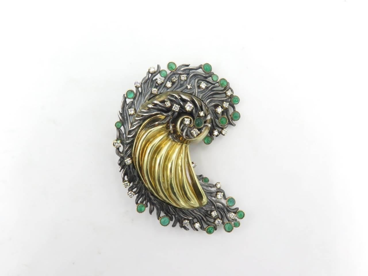 An 18 karat yellow gold, sterling silver, emerald and diamond brooch. Attributed to Marilyn Cooperman. Of paisley design. Centering a polished fluted gold panel, extending scrolling silver fringe, set with circular cut diamonds and round cabochon