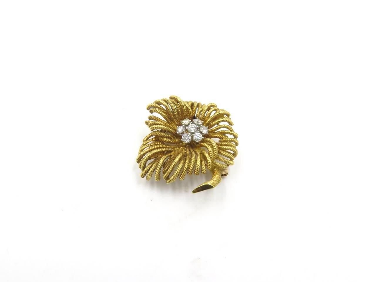 An 18 karat yellow gold and diamond brooch.  Van Cleef and Arpels. Circa 1960. Designed as a ropework flower, centering a circular-cut diamond cluster. Seven (7) diamonds weigh approximately 0.75 carat. Length is approximately 1 1/2 inches. Gross