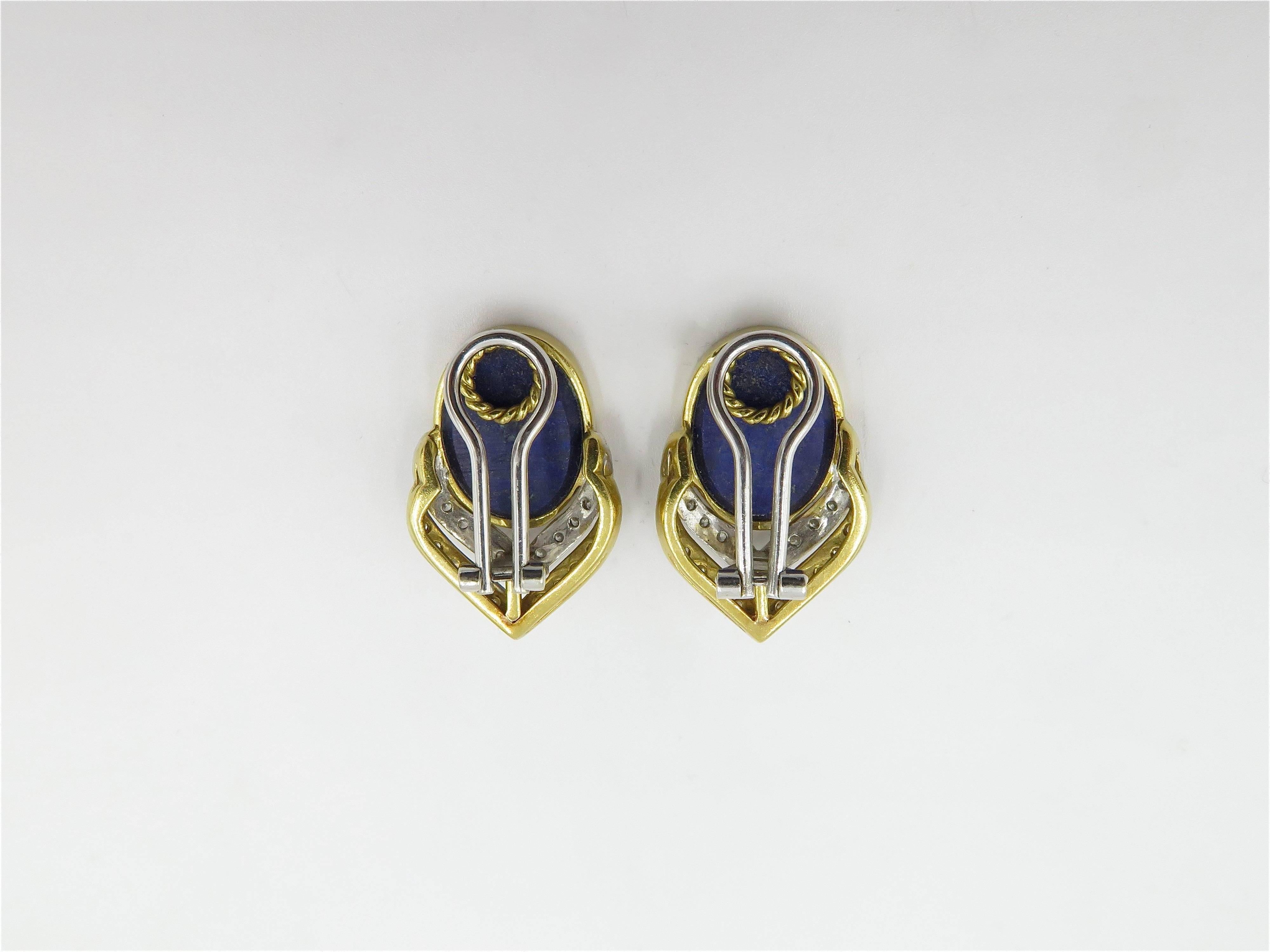 A pair of 18 karat yellow gold, white gold, lapis lazuli and diamond earrings. Italian. Each set with an oval lapis lazuli plaque, within a polished gold bezel, set to the bottom with pave set diamond V shaped motifs. Forty eight (48) diamonds weigh