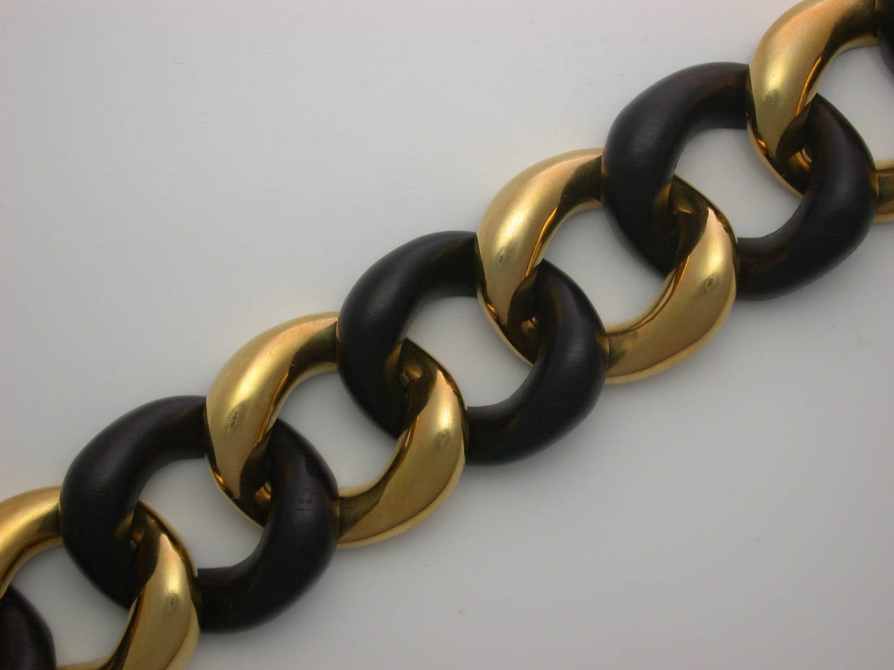 A Schepps classic, in the medium size (1 inch wide), designed as a straight row of polished yellow gold curb links alternating with carved dark chocolate brown rosewood links, beautifully flexible on the wrist, can be joined to form a choker