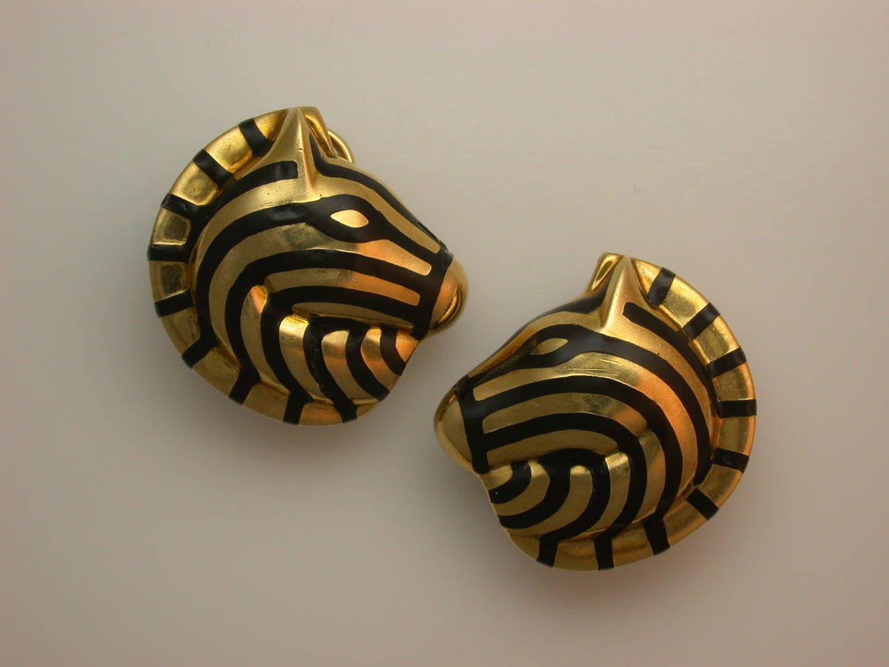 The handsome set consisting of circular pin and earclips, designed as polished yellow gold zebra heads in profile, with graphic striped black enamel detailing, the pin with horizontal single pin back and safety catch, the earclips with sturdy clip