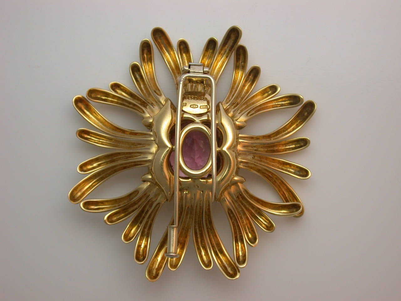 A lovely vintage brooch centering a faceted cushion-cut pink tourmaline, a bright, lively stone weighing approximately 20.95 carats, emanating polished yellow gold rays, with hinged double pin clip back and safety catch, signed Verdura, stamped 750