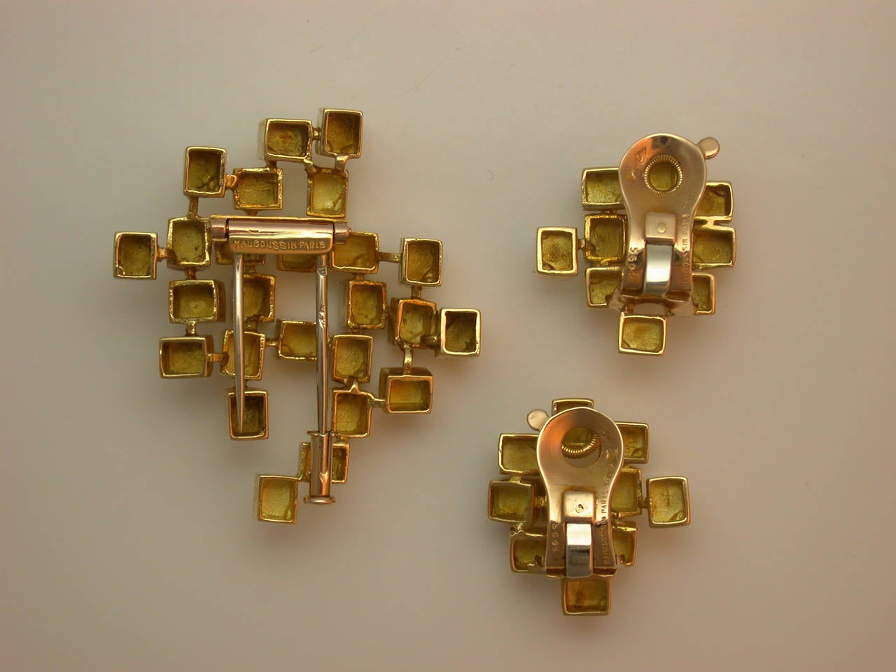Like a sculpture, assembled from polished and textured gold cubes, set on different planes to catch the light, consisting of a small clip brooch and small earclips, all signed Mauboussin Paris, numbered, with French maker's marks and French assay