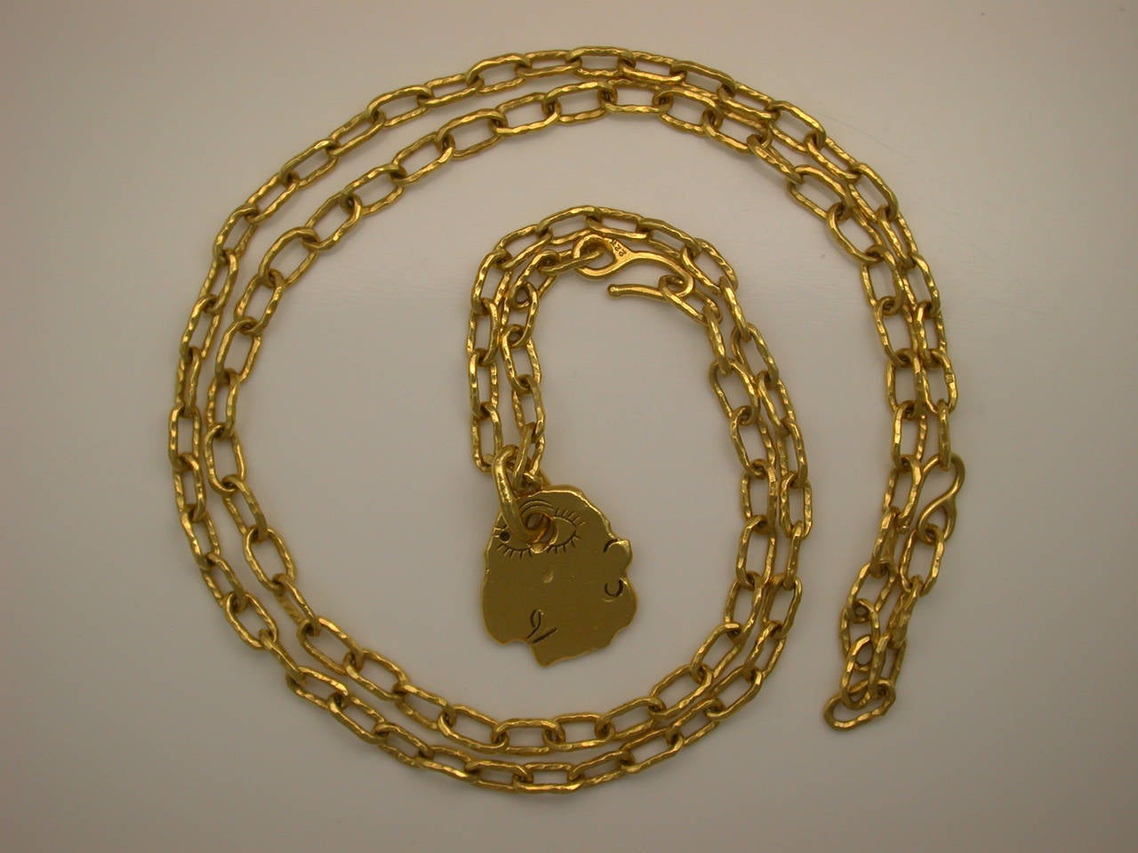 Two handmade hammered gold oval link chain necklaces (one 16 inches long with clasp, the other 19 inches long with clasp), signed JM in script for Jean Mahie, stamped 22K, joined to form a very long chain, with removable pendant designed as a face