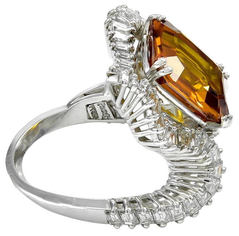The glamorous diamond cocktail ring by Piaget, Swiss, ca. 1965, centering an octagonal step-cut orange sapphire (12.67 x 10.69mm), pumpkin colored, weighing approximately 8.00 carats by formula, set within an asymmetrical platinum and diamond ribbon