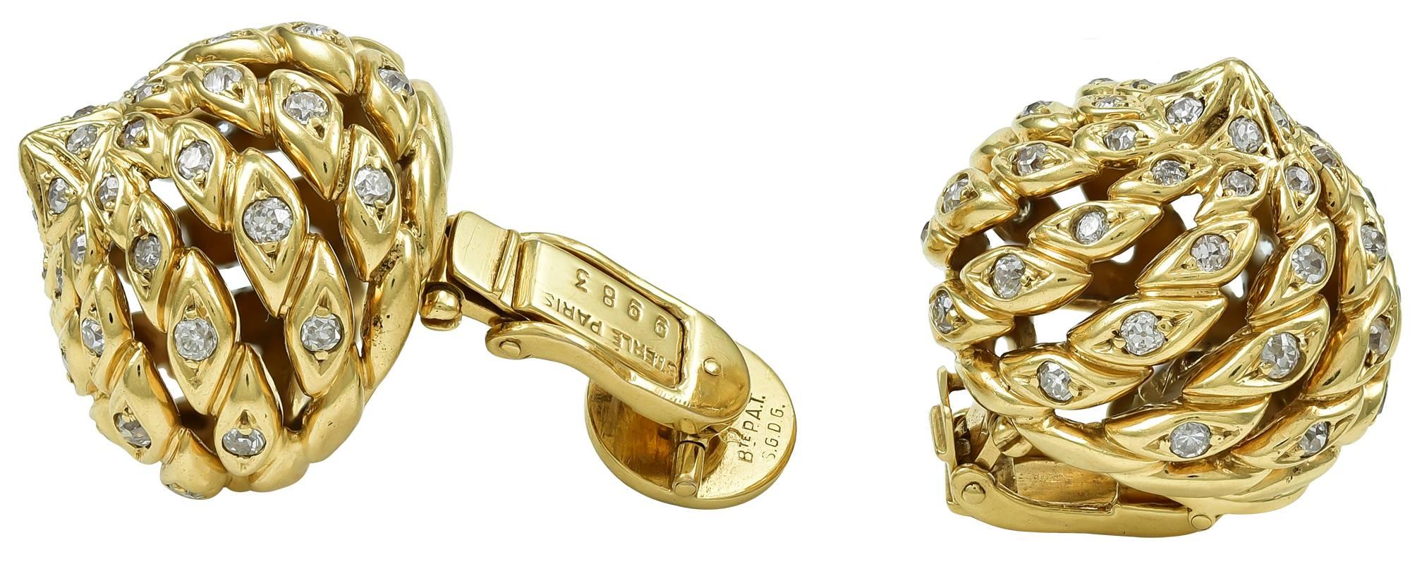 Three dimensional nut-shaped earclips designed as stylized gold and diamond ropes which rise from a circular base and swirl to a point (this motif is called 