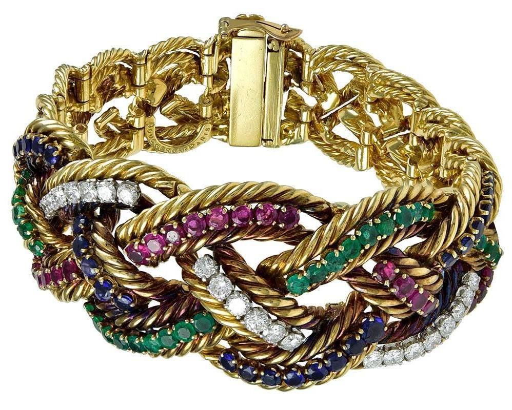 Designed as braided segments of twisted yellow gold rope, enhanced across the top with prong-set arcs of rubies, emeralds, sapphires and diamonds (approximately 2 1/2 carats each), tapering back flexibly to a secure lock and safety catch, signed