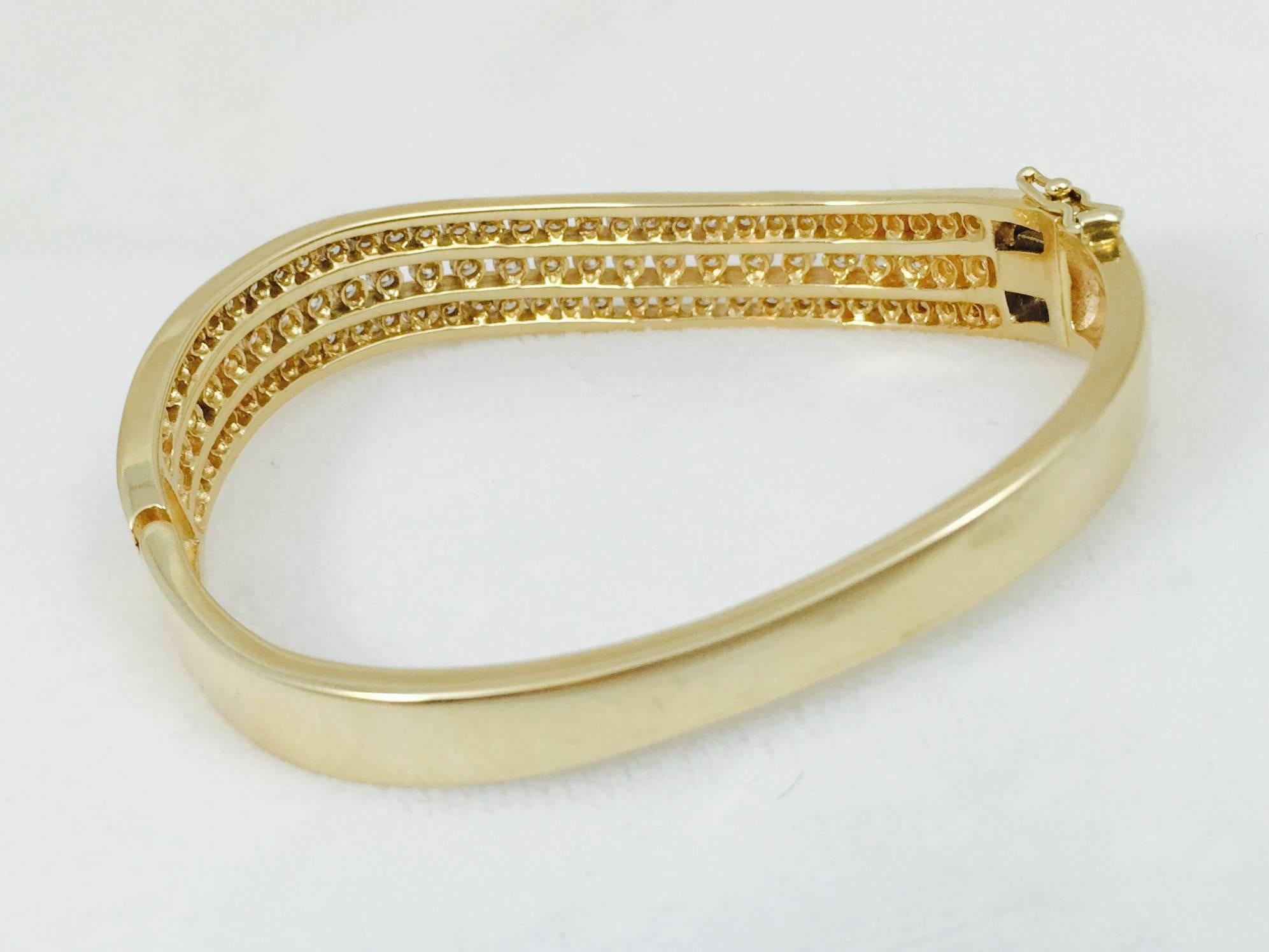 Fabulous diamond bangle crafted in 14 karat yellow gold.  Three wavy rows are loaded with channel set brilliant cut diamonds having an approximate total weight of 3.56 carats.  G color.  VS1 clarity.  Secure clasp with additional figure eight safety