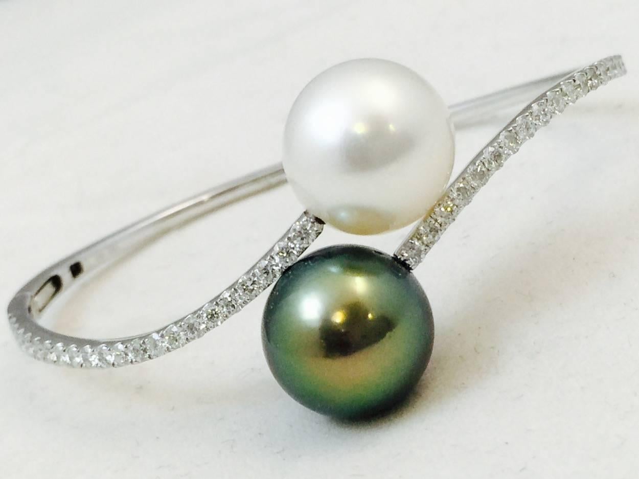 Masterfully created in 18 karat white gold.  Stunning by-pass design features one black and one white cultured Tahitian Pearl measuring 12-13MM each.  Beautifully accented with 42 brilliant cut diamonds weighing 1.03 carats total.  G-color, VS