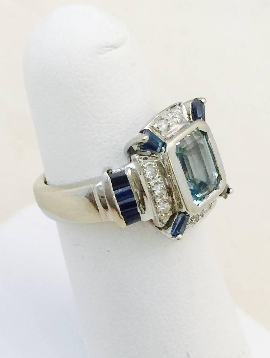 Crafted in 14 karat white gold, this fantastic Art Deco style ring looks like tomorrow's heirloom!  Centered by a bezel set, emerald cut aquamarine weighing 2.36 carats, the design incorporates 4 tapered baguette cut blue sapphires and 8 baguette,