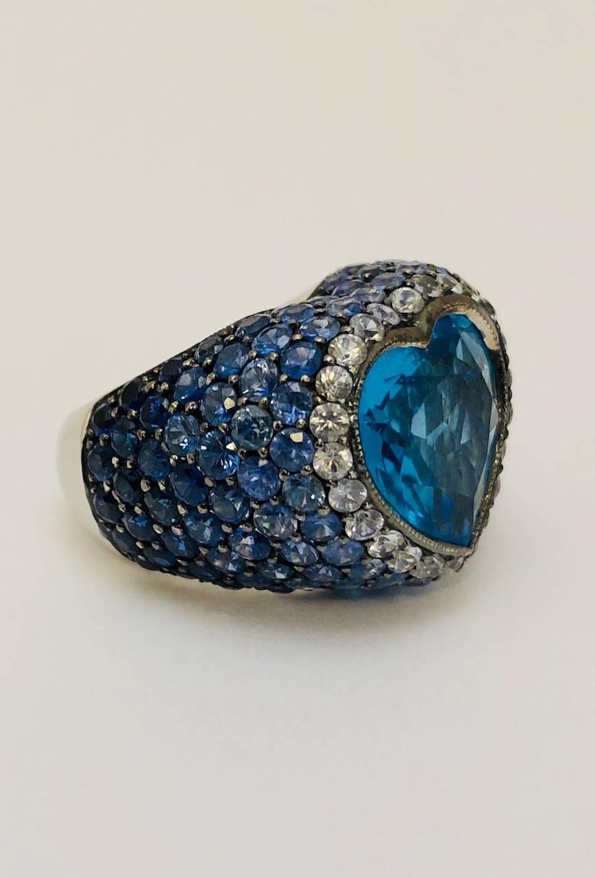 Romance is alive and well in this ring!  Heart shape is perhaps the most endearing and enduring design in all of jewelry.  Beginning with fine 18 karat white gold, this ring has an impressive 9.04 carat heart shape faceted blue topaz.  Framing the