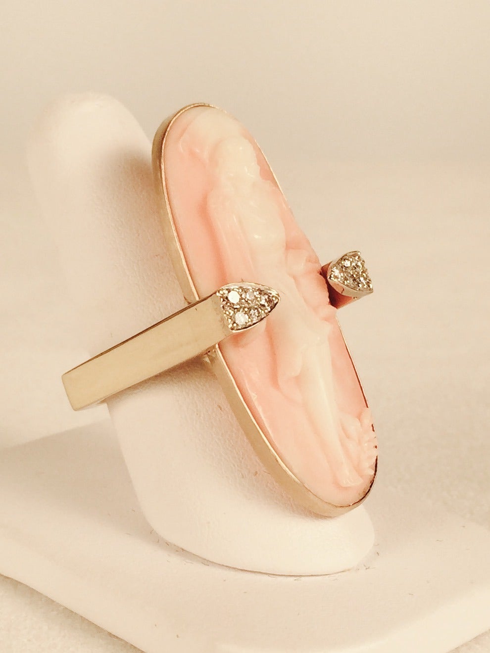 Delicately carved lady in bezel set Pink Coral distinguishes this ring from the rest!  Two prong-like enhancements contain 10 brilliant cut diamonds approximately .50ct total weight.  Size 7 with soldered sizing spring.  Squared-off shank prevents