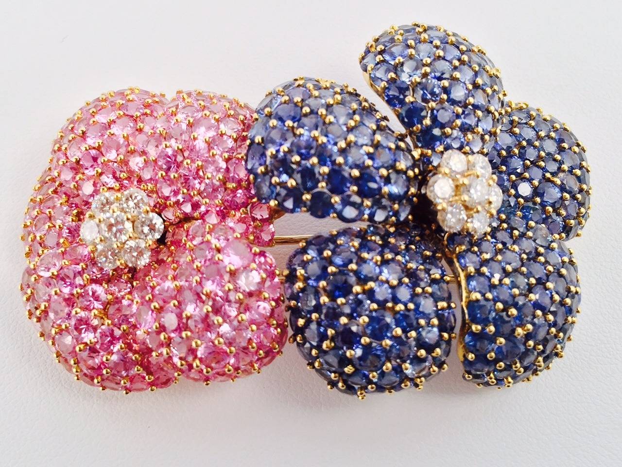 Set in 18K Yellow Gold, Pink and Blue Sapphire Double Flower Brooch features exquisite white diamond detail!  Pink Sapphires: Approximately 16.82 ct tw.  Blue Sapphires:  Approximately 26.24 ct tw.  White Diamonds:  Approximately 1.40 ct tw.  Stone