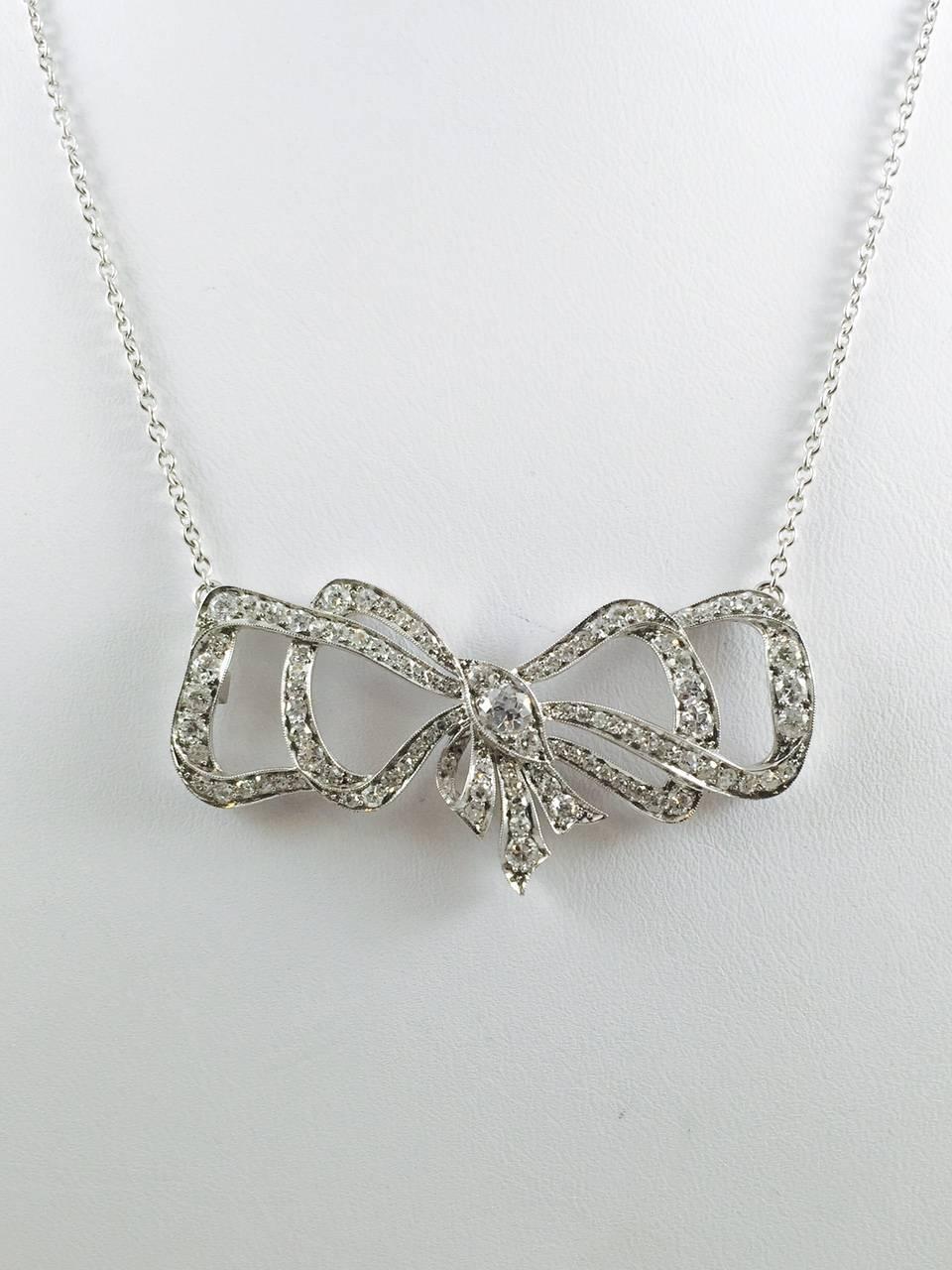 Masterfully created in Platinum.  Curves, twists and turns form the prominent bow centerpiece filled with brilliant cut diamonds. Every edge of the bow is finished with milgrained edges.  Milgrain literally means 