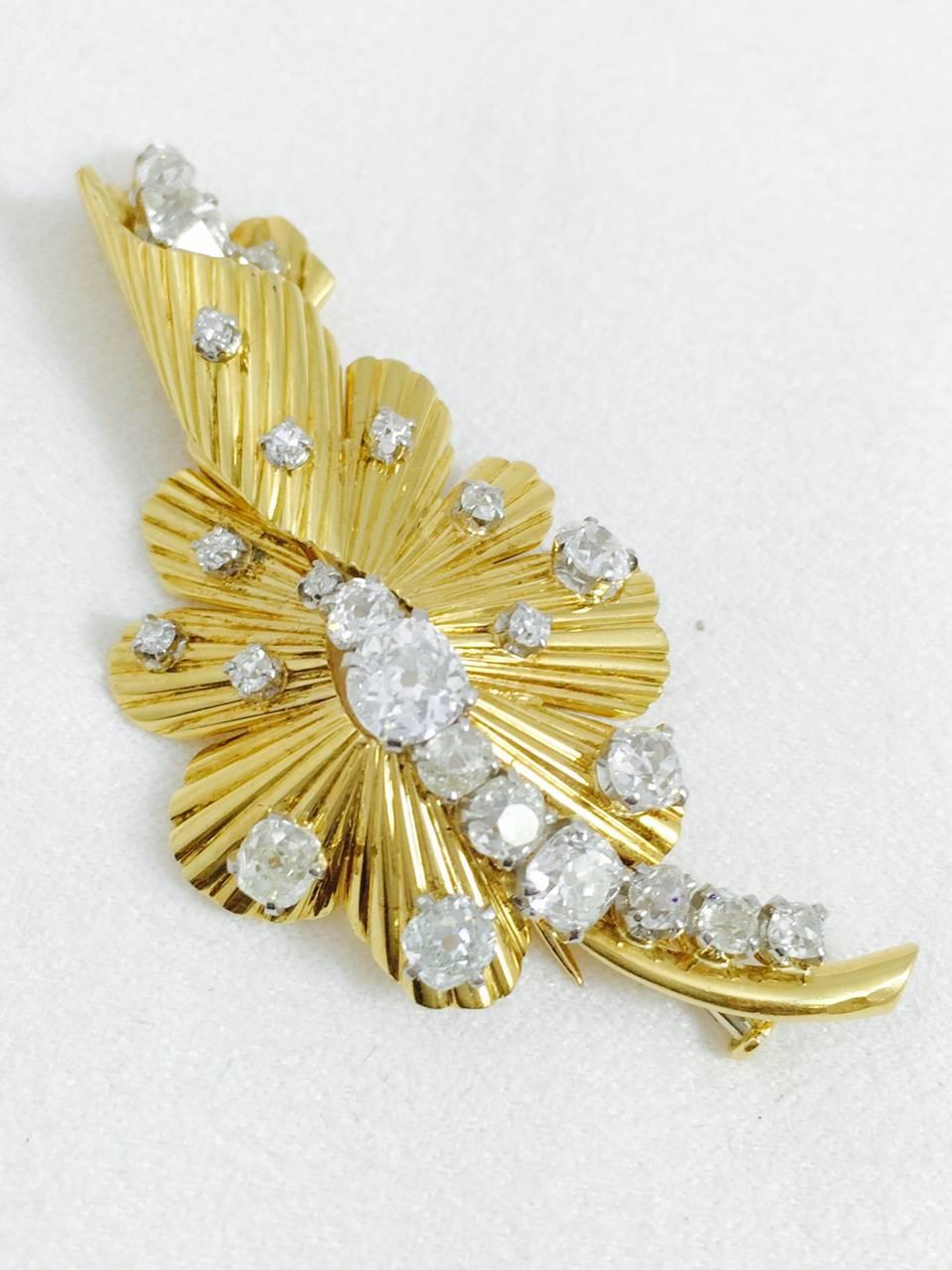 Artful ribbon work in 18 karat yellow gold forms the base for this stylish flower brooch.  An impressive approximate 5.50 carats total weight  of European Cut diamonds having E color, VS1 clarity.  Fantastic design.  Fabulous sparkle.  Brooches have