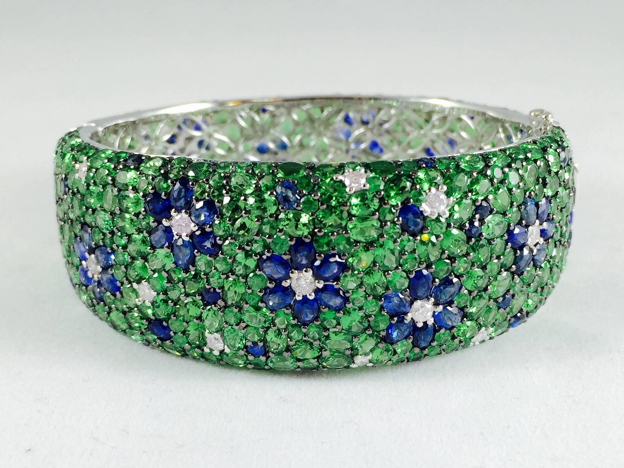 A more stunning bracelet cannot be found! Crafted in 18 Karat White Gold.  A green sea of Tsavorites flows all the way around the entire piece.  Thirteen Blue Sapphire flowers float effortlessly along top and bottom.  Diamonds dot the bracelet and