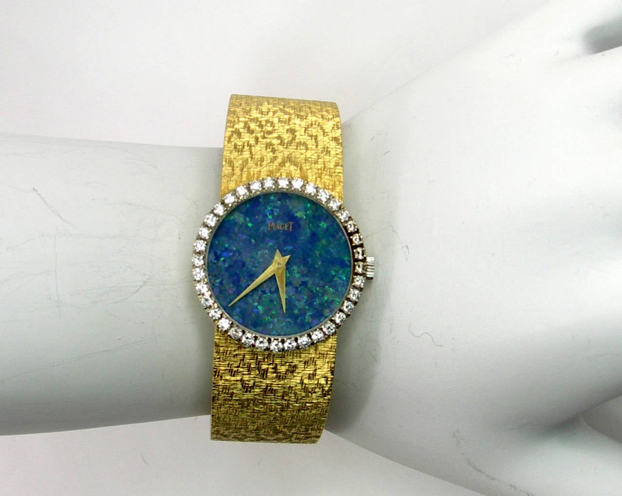 One ladies 18K yellow gold Piaget wristwatch centered around a magnificent opal dial. The bezel measures 24mm in diameter and is set with a total of approximately 1ct of round brilliant cut diamonds. The overall length is 6 and 1/8 inches, and the