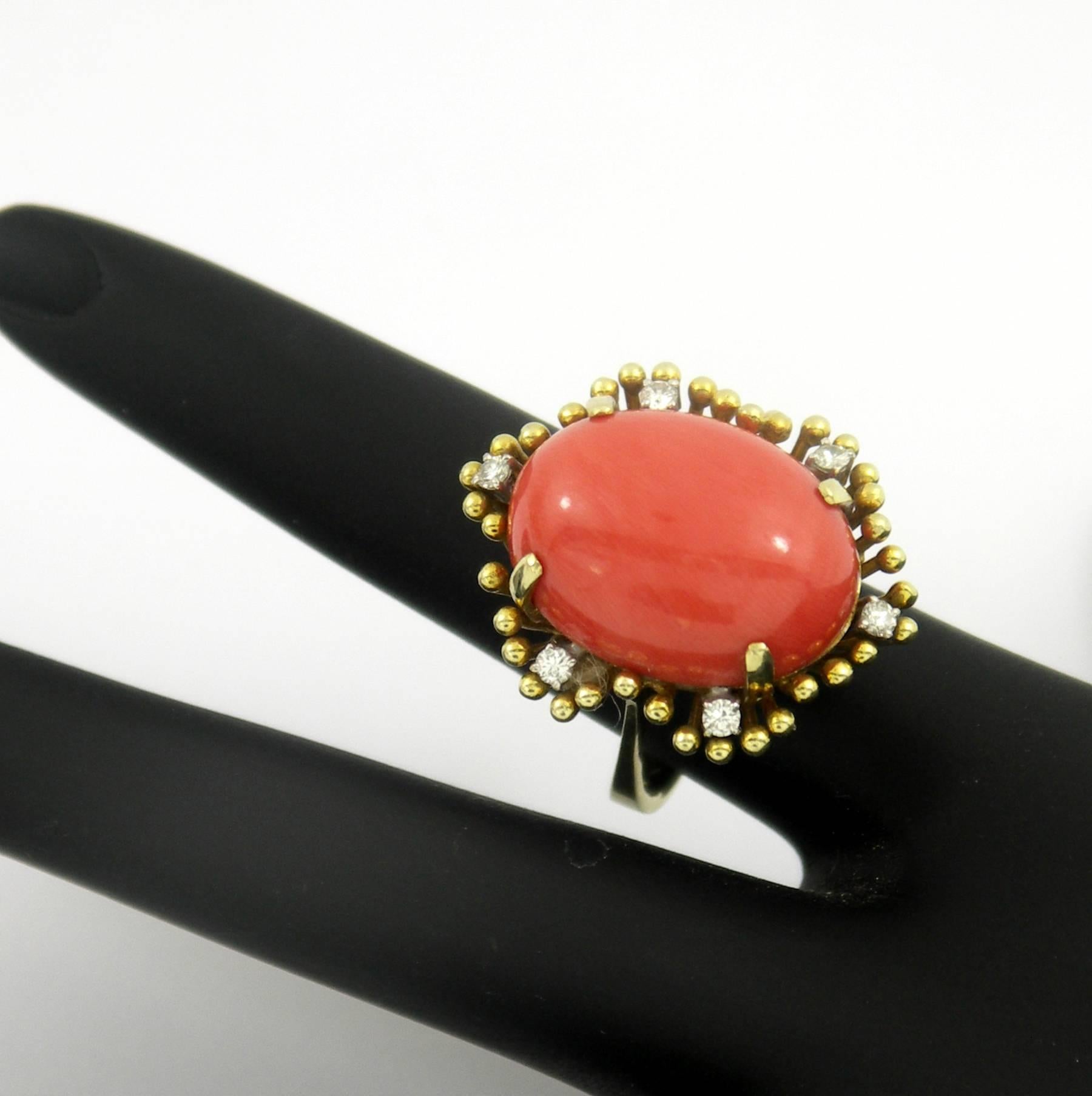 A ladies mid-century 14K yellow gold ring set with one oval coral measuring 20mm X 15mm. The ring incorporates an almost floral design with beaded gold posts that resemble the stamens of a flower or a starburst. There are six diamonds positioned