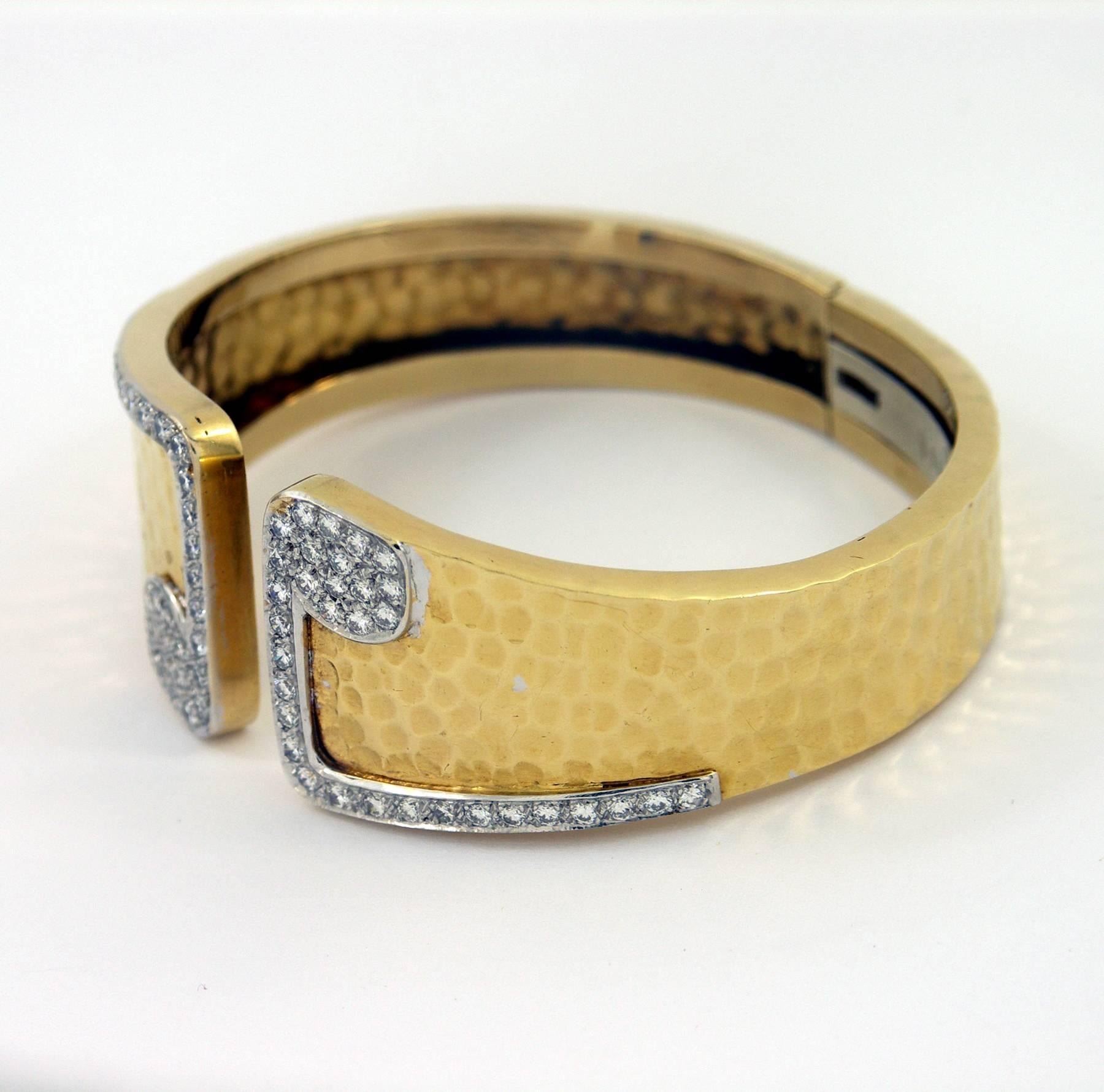 A ladies 18K yellow gold hammer finished bracelet measuring 1 inch at the opening and tapering down to 1/2 inch at the hinge. The split front features mirror imaged motifs, pave' set with a total of approximately 1ct, round brilliant cut diamonds.