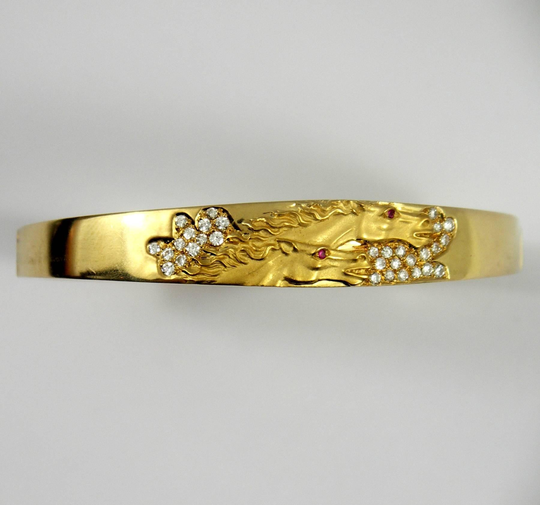 An 18K yellow gold hinged bangle bracelet by Carrera y Carrera, featuring two horse heads in profile, with ruby eyes. The 