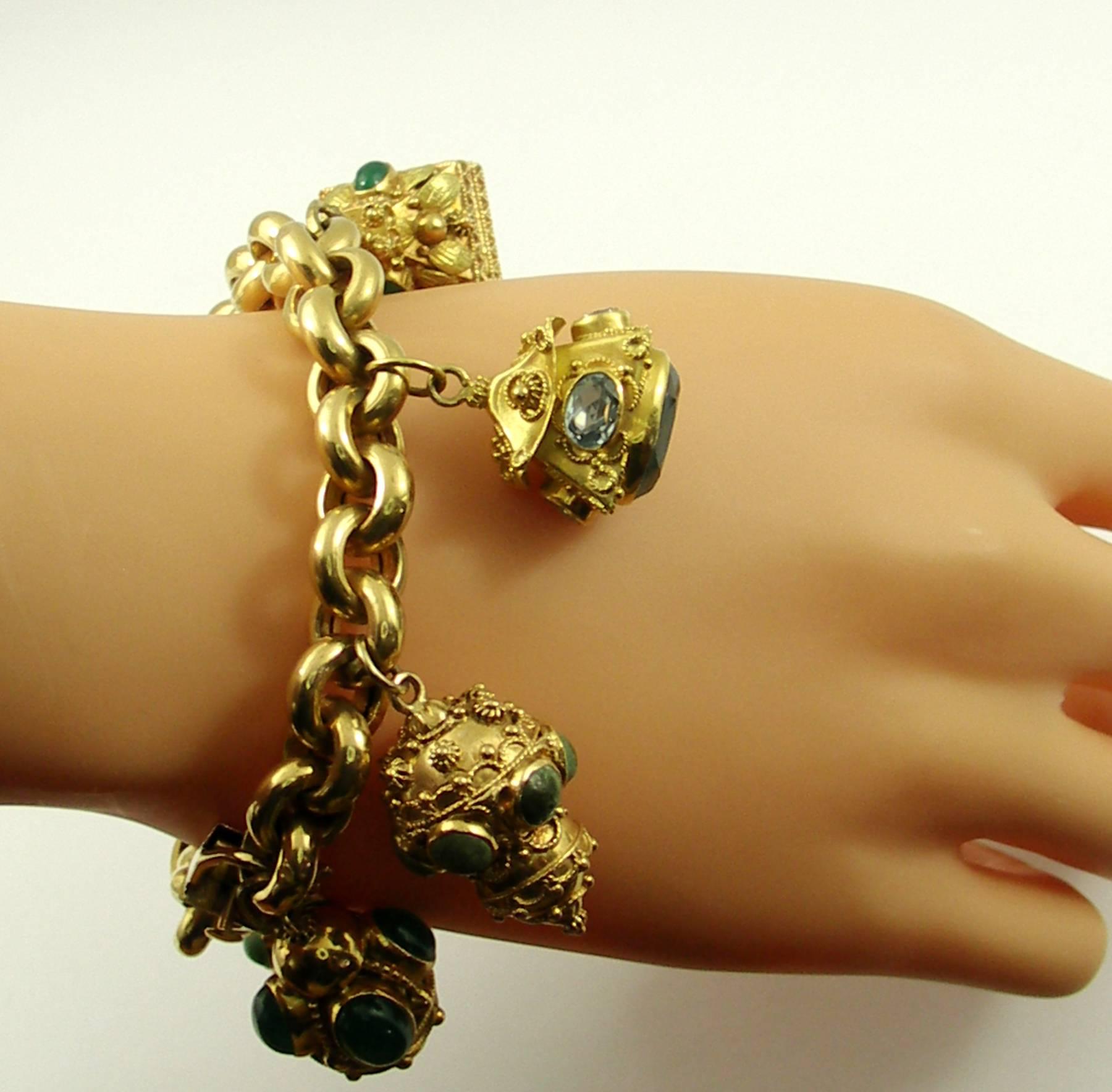 An 18K yellow gold charm bracelet, comprised of one cable link bracelet measuring 7 3/4 inches long and just under 1/2 an inch wide, attached are nine Etruscan revival charms, set with an assortment of semi-precious stones, pearls, and glass.