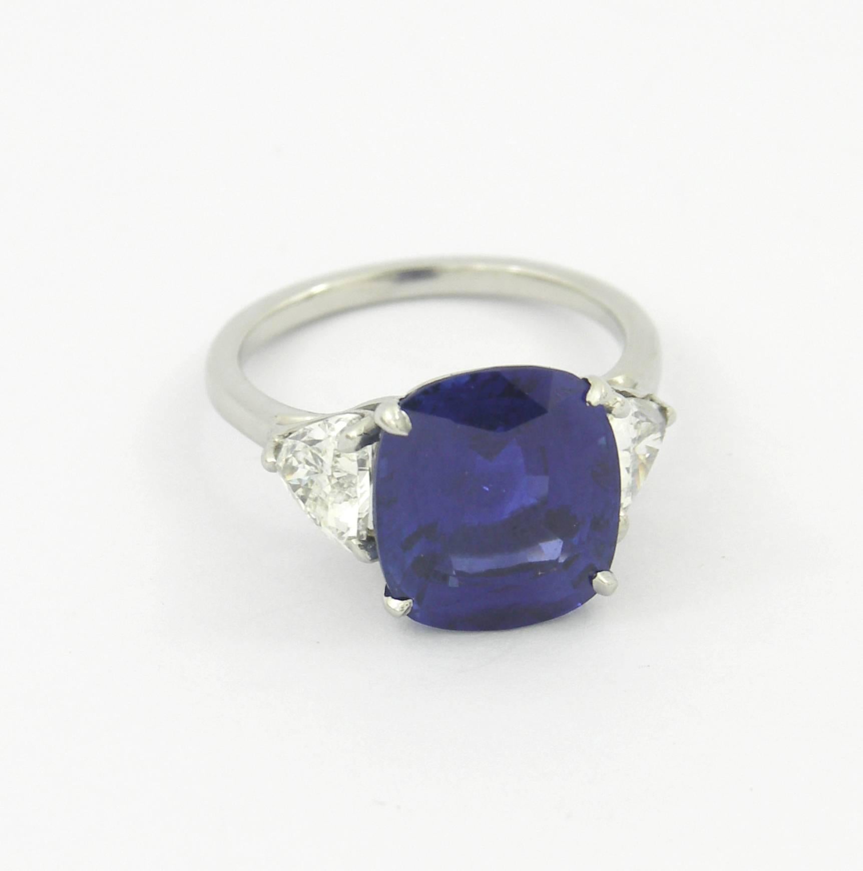 A hand made platinum ring centered around a 7.32ct cushion cut sapphire, with a trilliant cut diamond on either side, for a three stone inspired look. The Sapphire is described in an A.G.L. certificate as being of Ceylon origin, and is a vibrant