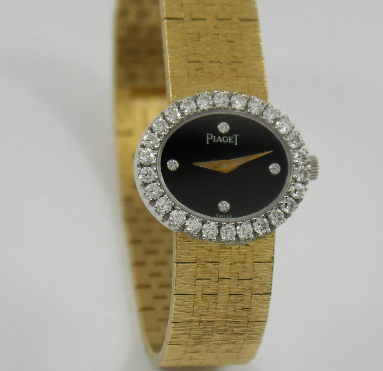 One 18K yellow gold wristwatch by Piaget featuring a bezel measuring 19mm long, and 22mm wide, with an onyx dial set with round brilliant cut diamonds at the 12:00, 3:00, 6:00, and 9:00 positions. Measuring 6 1/4 inches long, this watch features a