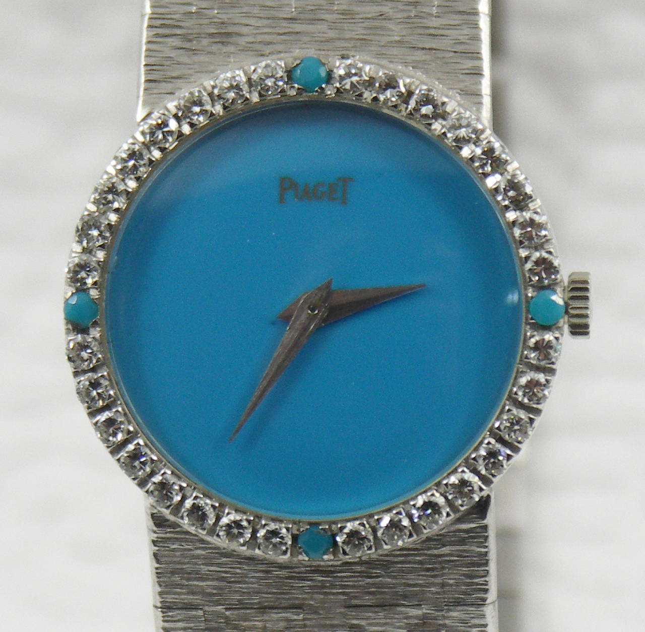 One ladies 18K white gold Piaget wristwatch with turquoise dial. The bezel of this fine timepiece measures 24mm in diameter, and is set with 4 cabochon turquoise and 32 round brilliant cut diamonds weighing 0.85ct total approximate weight. The blue