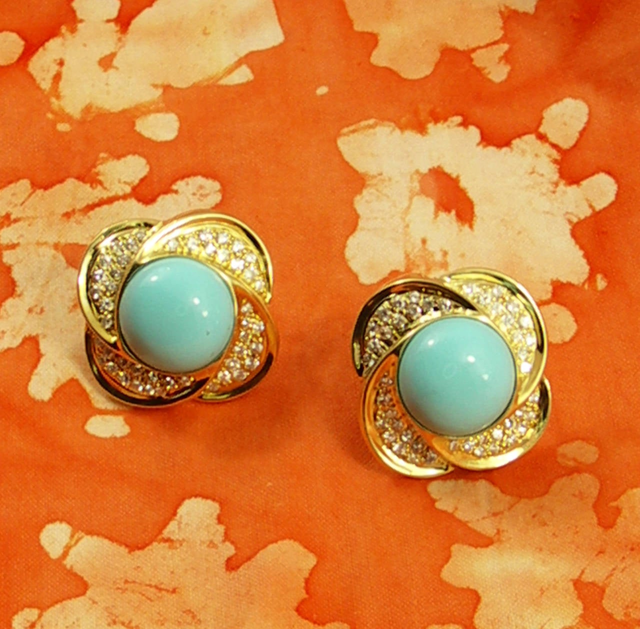 A pair of 18K yellow gold earrings, each set with a round cabochon turquoise, measuring 16mm. Surrounding the turquoise are four sections arranged in a floral design, and pave' set with round brilliant cut diamonds. These beautiful earrings measure