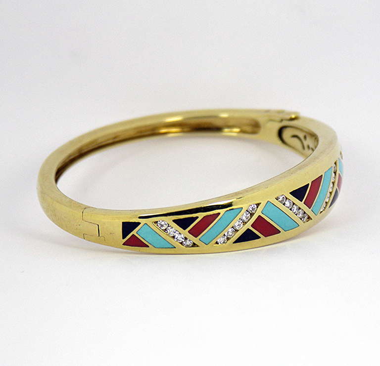 A 14K yellow gold bracelet by Asch Grossbardt, tapering in width from 3/16 of an inch up to 1/2 inch. This bracelet is beautifully inlaid with stylish, angular pieces of coral, onyx, and turquoise. In between the contrasting colored stones are six