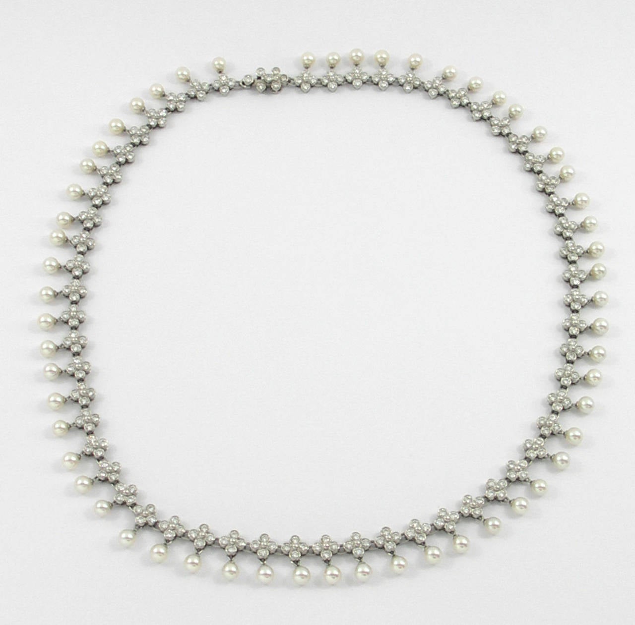 A ladies necklace by Tiffany & Company, comprised of platinum, diamonds, and pearls. Measuring 3/8 of an inch wide, each link is comprised of a clover of four round brilliant cut diamonds, and a 4mm round cultured pearl. Diamonds weigh 5ct total
