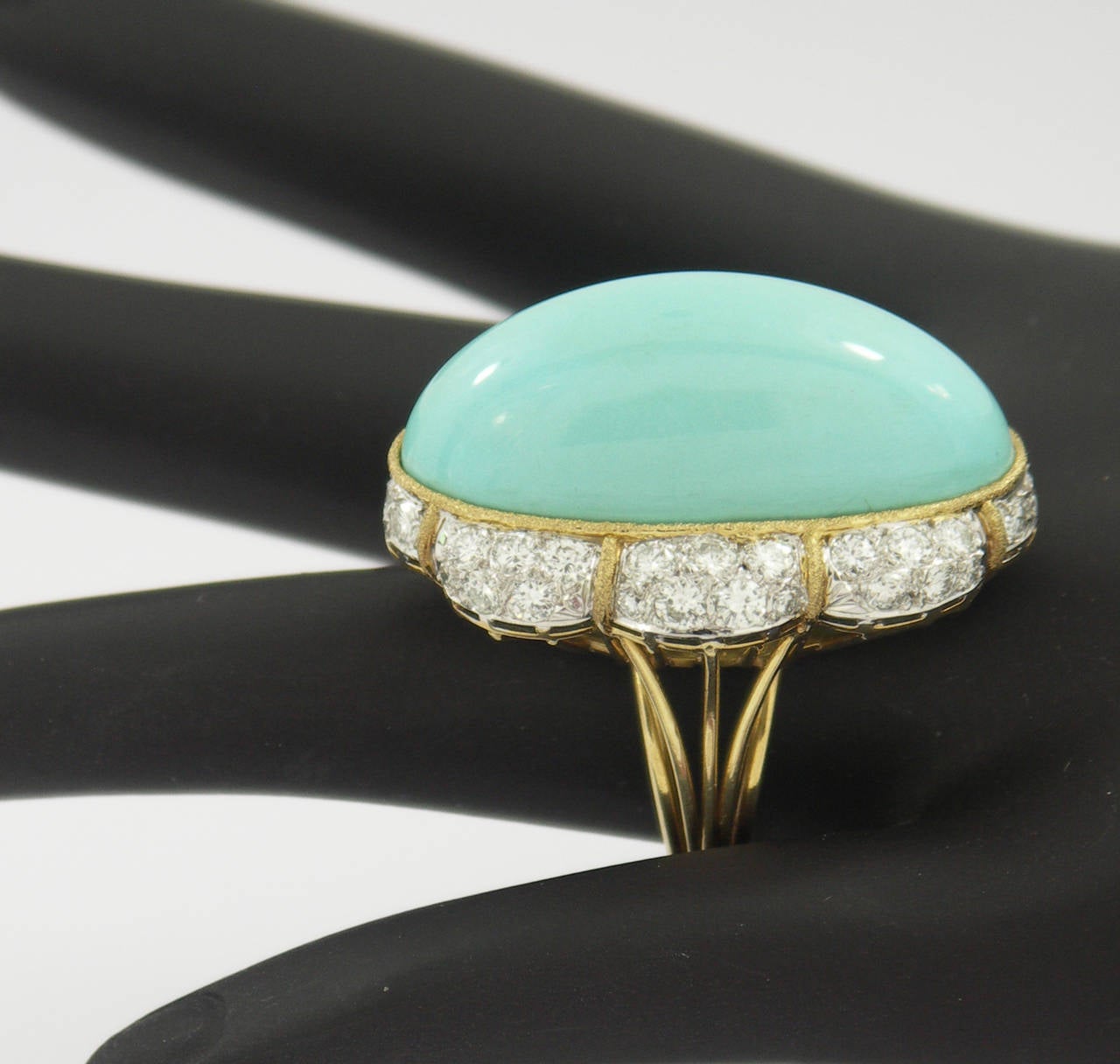 One ladies 18K yellow gold cocktail ring measuring approximately 0.88 inches long by 1 inch wide. This sleek and slender ring is set with a cabochon turquoise measuring 40mm long and 16mm wide. Surrounding the turquoise are 48 round brilliant cut