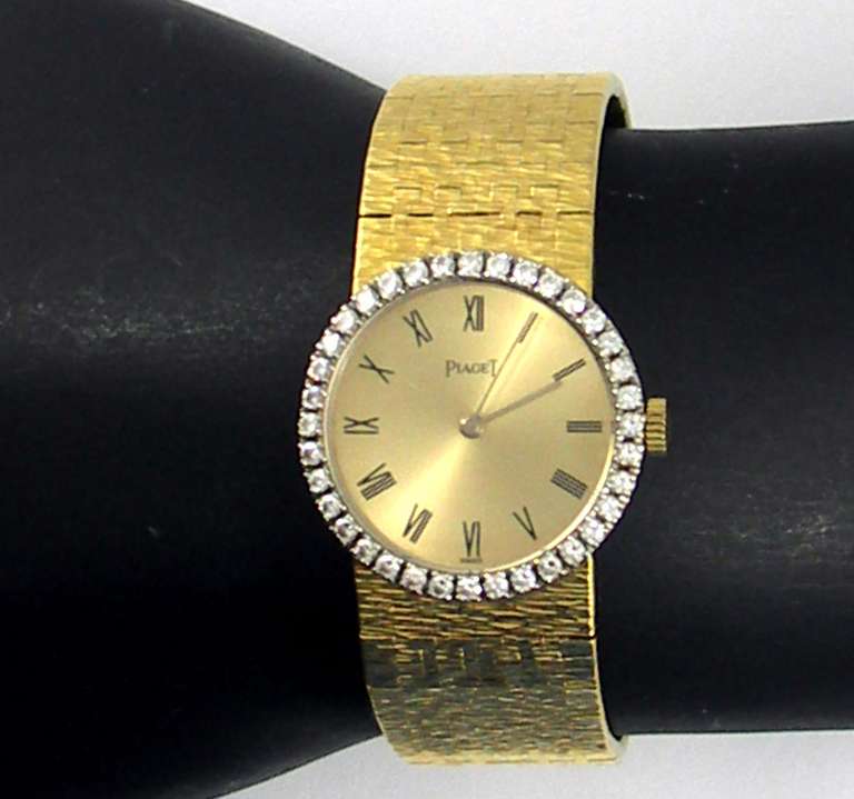 Piaget lady's 18k yellow gold bracelet watch with diamond-set bezel. This wonderful Swiss watch features a champagne dial with Roman numerals. Surrounding the dial are 36 round brilliant cut diamonds weighing approximately 1 ct total weight.