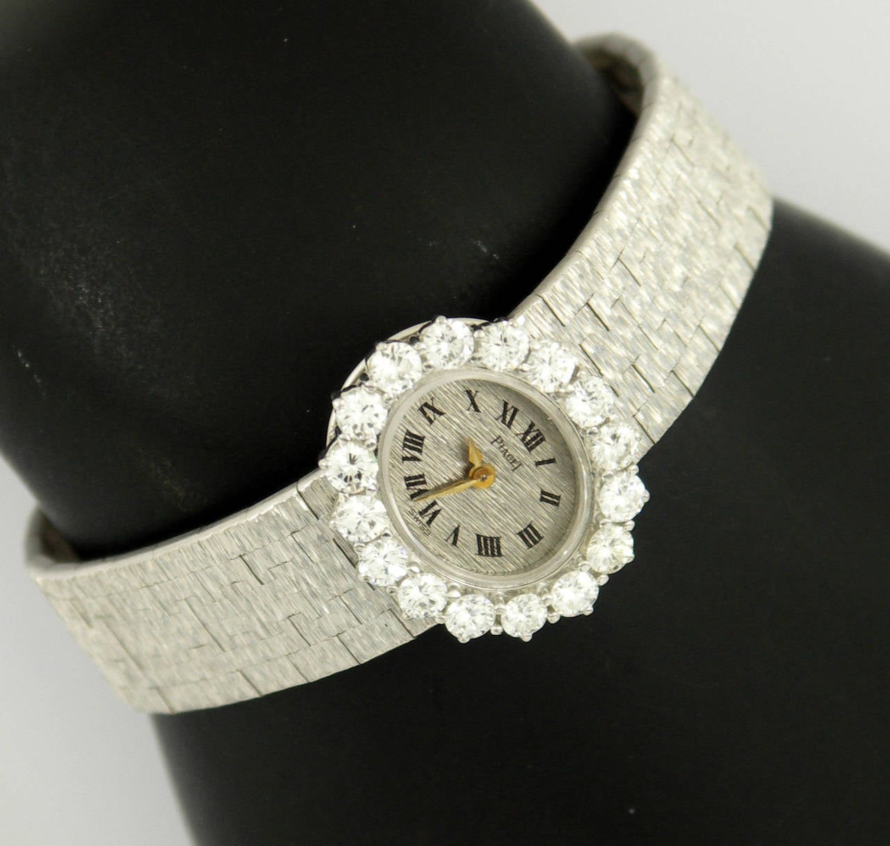 An 18K white gold ladies Piaget wristwatch, with white gold dial and black, Roman numerals. Surrounding the watch is a bezel set with 16 round brilliant cut diamonds, weighing 2.33ct total approximate weight. The bezel measures 20mm X 24mm, and the