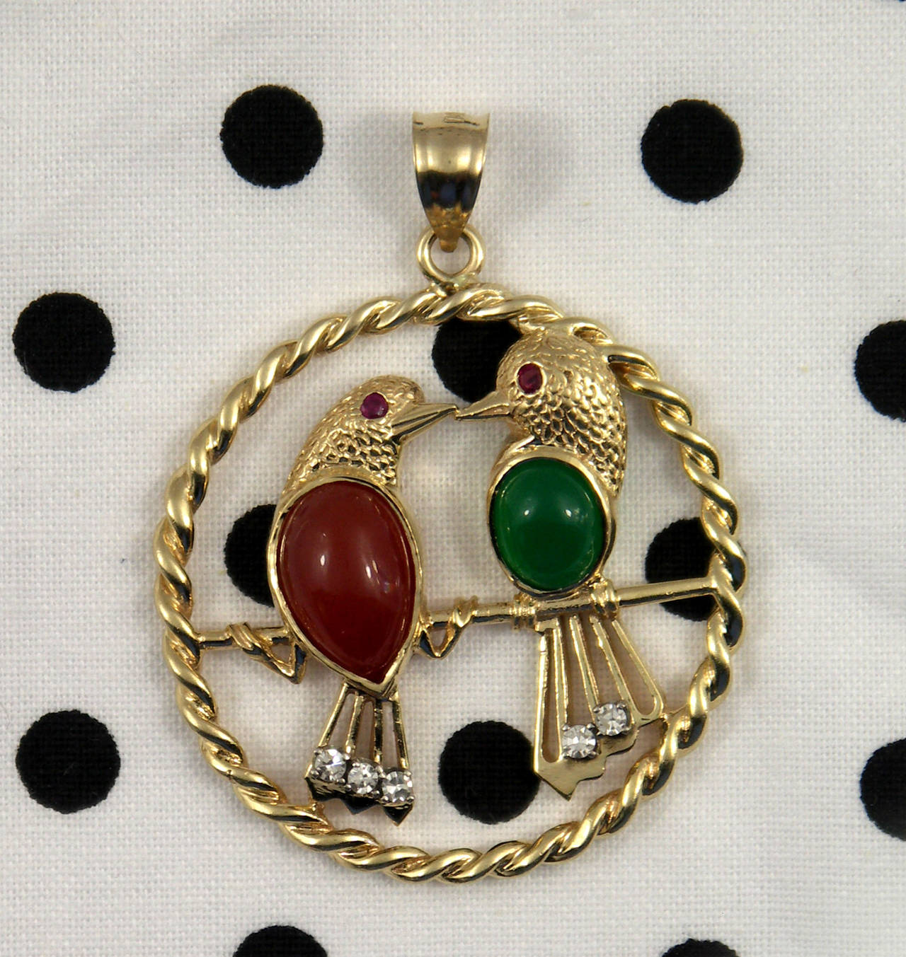 A 14K yellow gold pendant featuring two lovebirds, one set with a carnelian belly, the other with a chrysoprase belly. Each bird has a ruby eye, and one is set with three diamonds in the tail, while the other has two diamonds, for a total