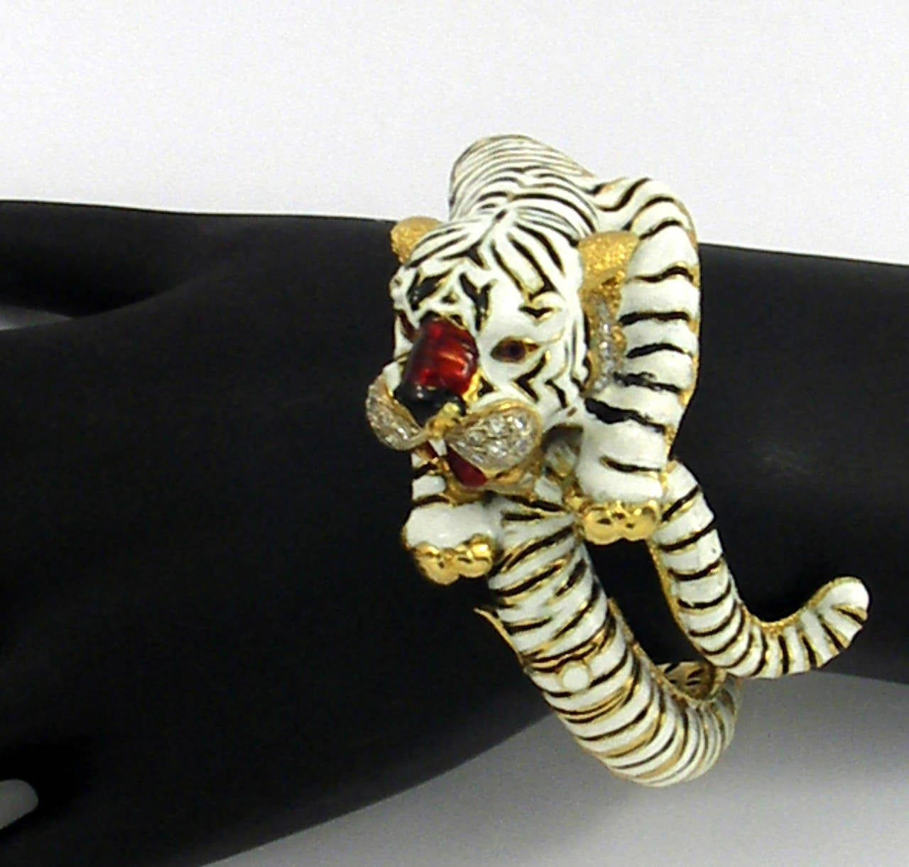 18K yellow gold bangle bracelet featuring a tiger design with black and white enamel stripes, diamond face, and ruby eyes. With a 6 3/4 inch circumference, this animated bracelet will fit a medium wrist.