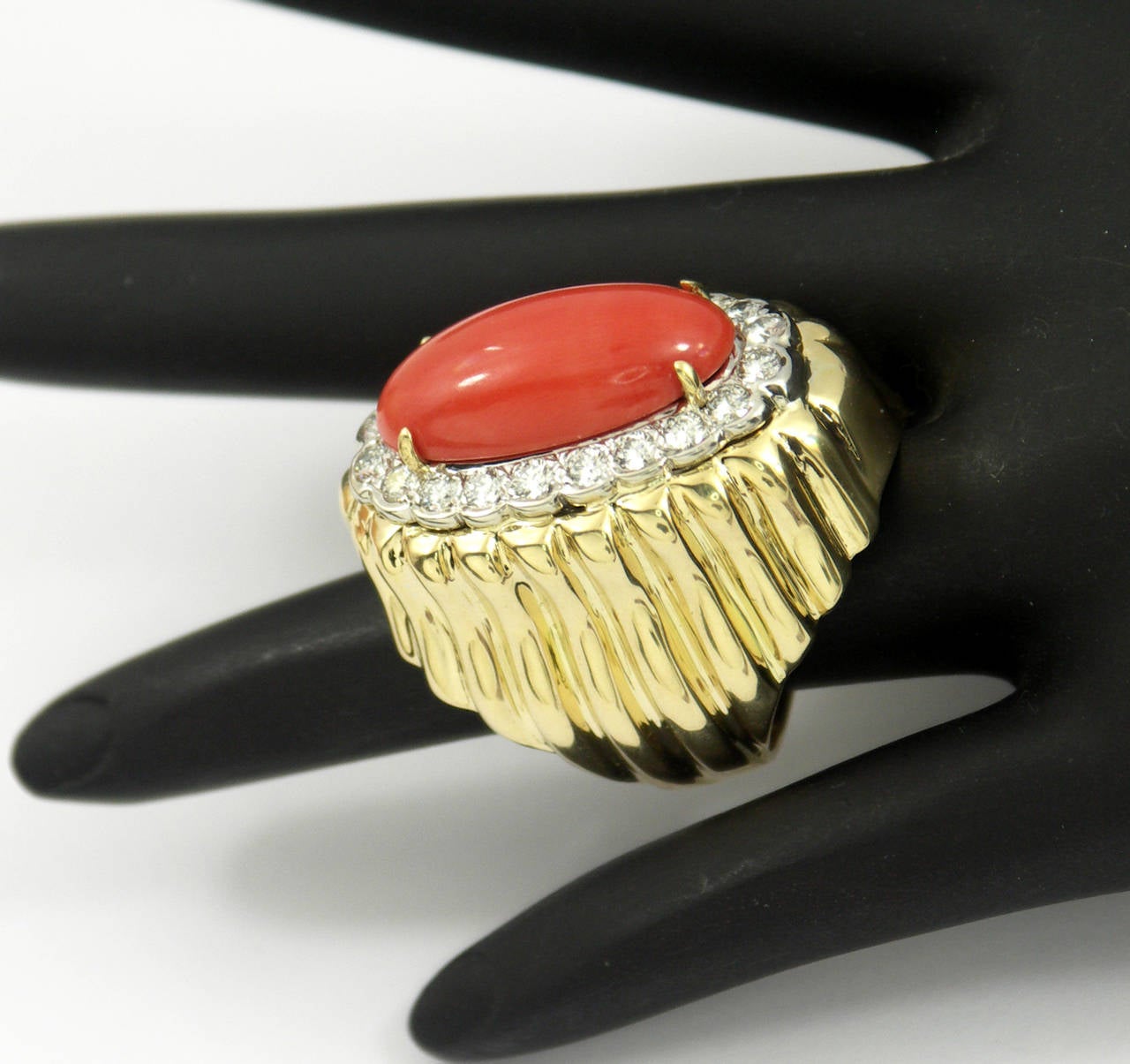 An 18K yellow gold ring set with one oval cabochon coral measuring 22mm X 12mm. Surrounding the coral are 20 round brilliant cut diamonds set in a white gold plate weighing 1.5ct total approximate weight. Ring size 6 1/2