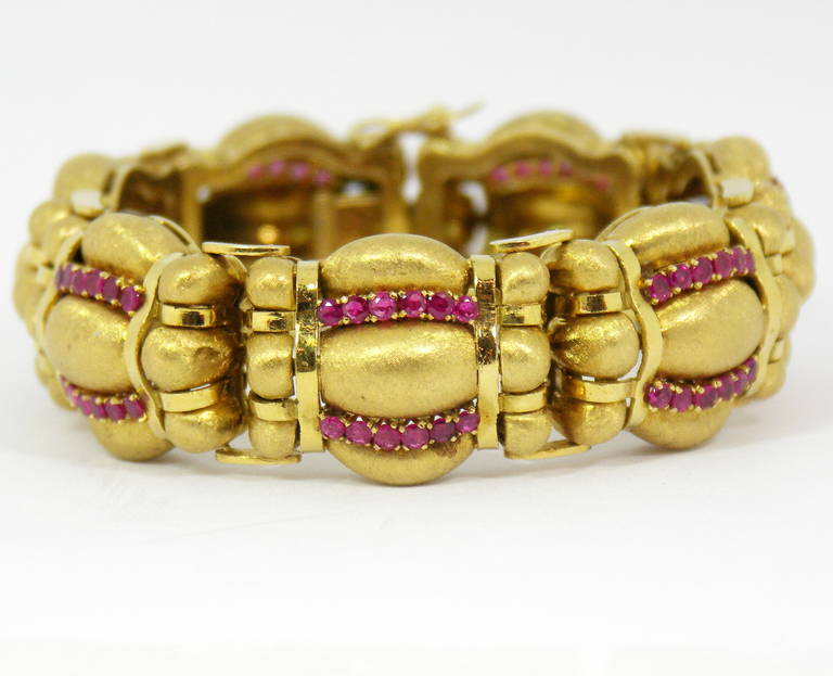 A beautifully finished 18K yellow gold bracelet, featuring a rounded design, and strips of round, faceted rubies. Each link features a Florentine finished design, which appears as though it were bunched by high polished gold straps. Each of the