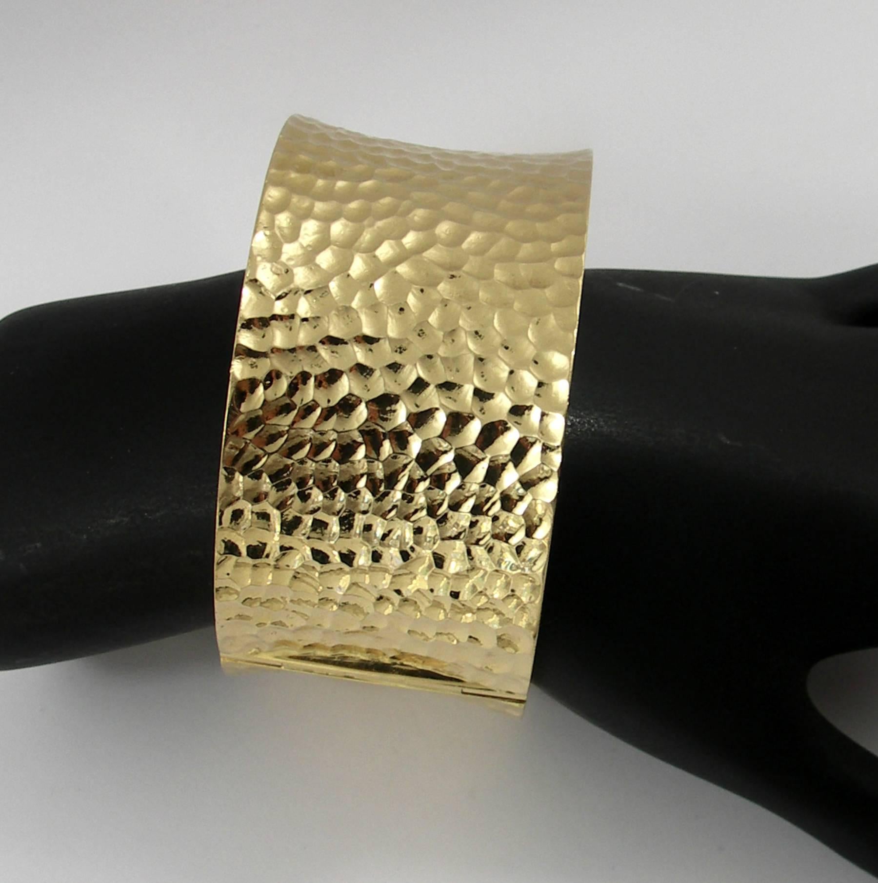 A 14K yellow gold bracelet, measuring 1 1/2 inches wide, and featuring a deep hammered finish. Bracelet is solidly built, with a hinge for easy access, and measures 7 inches in circumference.  Weight 107 grams.
