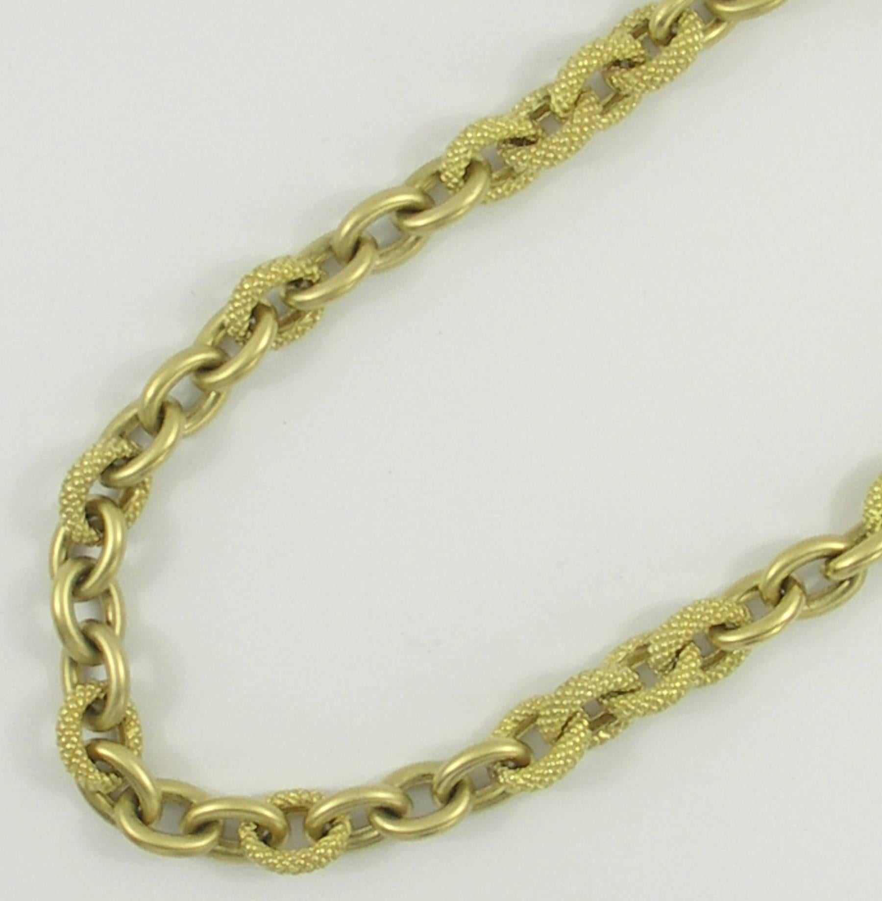 An 18K yellow gold necklace, with a design of alternating sections of 3 links per section, with sections alternating between a texture finish, and a satin finish. Each link measures 10mm in width, and the necklace features two signature