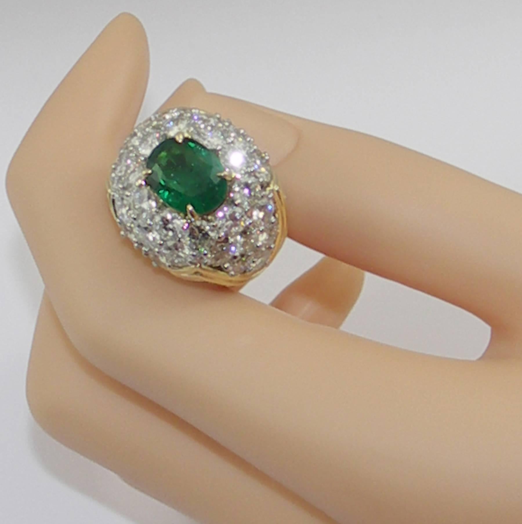  One ladies 18 karat yellow gold and platinum cocktail ring, centered around one oval faceted emerald weighing approximately 2 1/2 carats, with a lively green tone and excellent saturation. Surrounding the emerald are round brilliant cut diamonds
