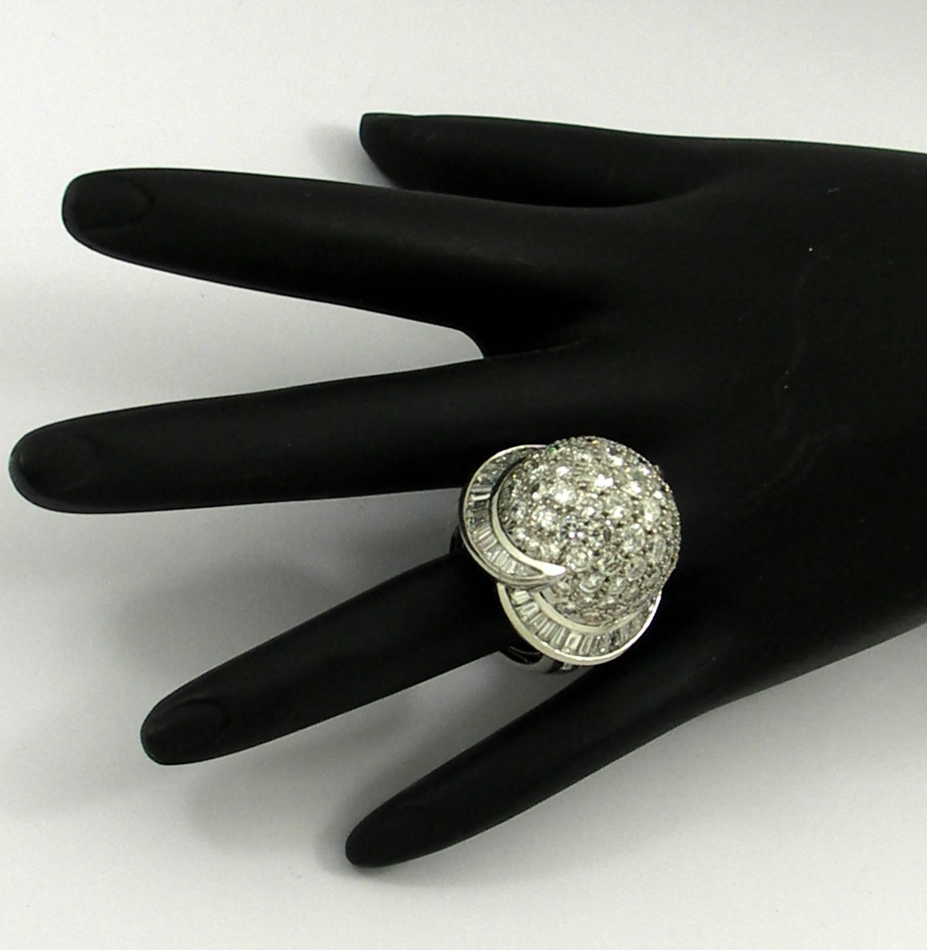 A modern design ring incorporating upswept bands of baguette cut diamonds around a pave' diamond dome. This platinum cocktail ring also features baguette and round cut diamonds on the shoulders for a total approximate weight of 9ct. Diamonds are of