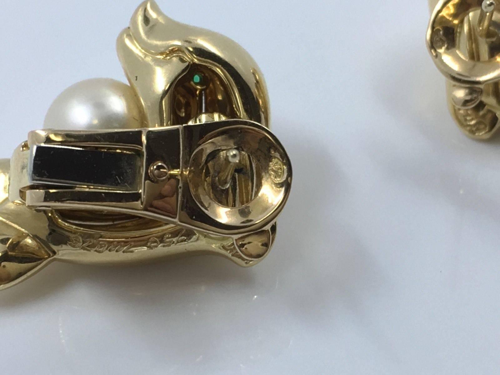 Cartier Dolphin earrings, composed of an 18k yellow gold dolphin,
accented by a round pearl, with circular-cut emerald eye, with clip and post backs.

numbered 711076, signed Cartier.
23mm length and 18mm width.
